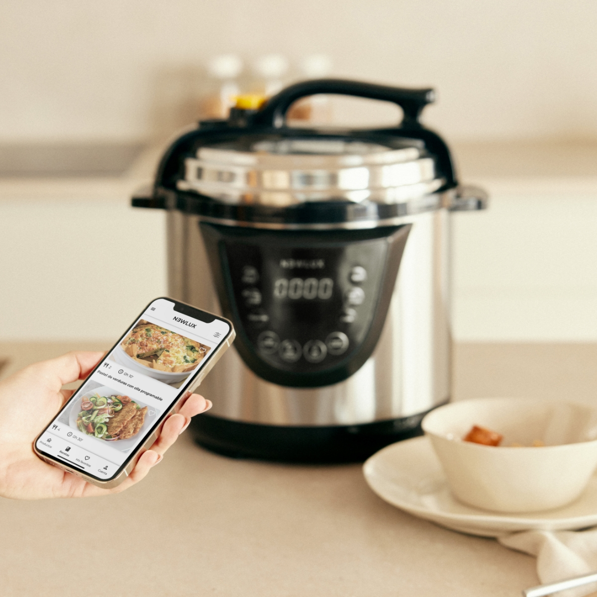 Persona sostiene teléfono con receta, olla a presión en el fondo.
