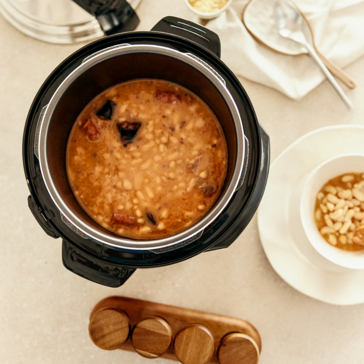 Vista aérea de una olla a presión con frijoles, especias en soporte de madera.
