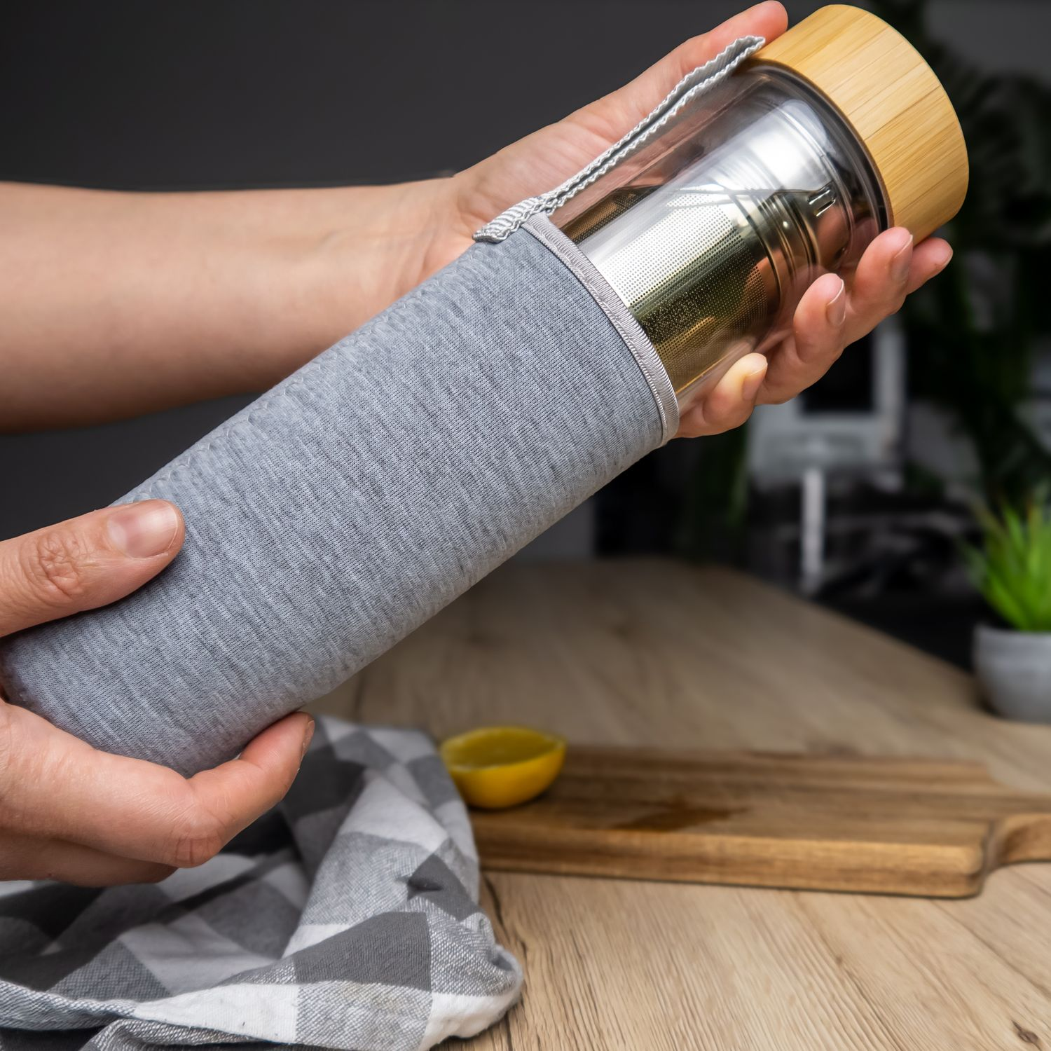 Hände halten eine grau stoffbezogene, isolierte Wasserflasche mit Holzdeckel.