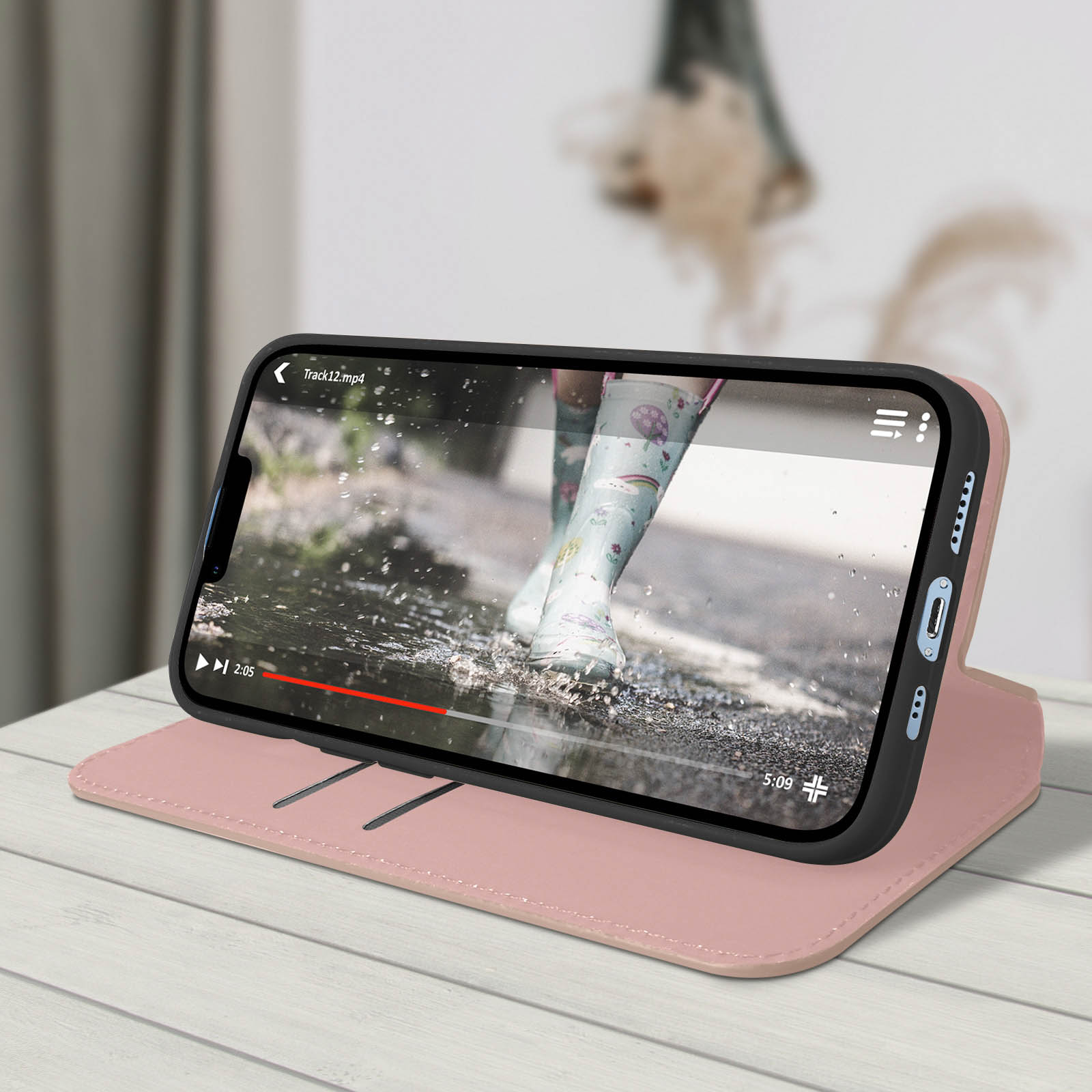 Telefoon op een roze hoes, toont een video van laarzen in plassen. De hoes ligt op een houten tafel.