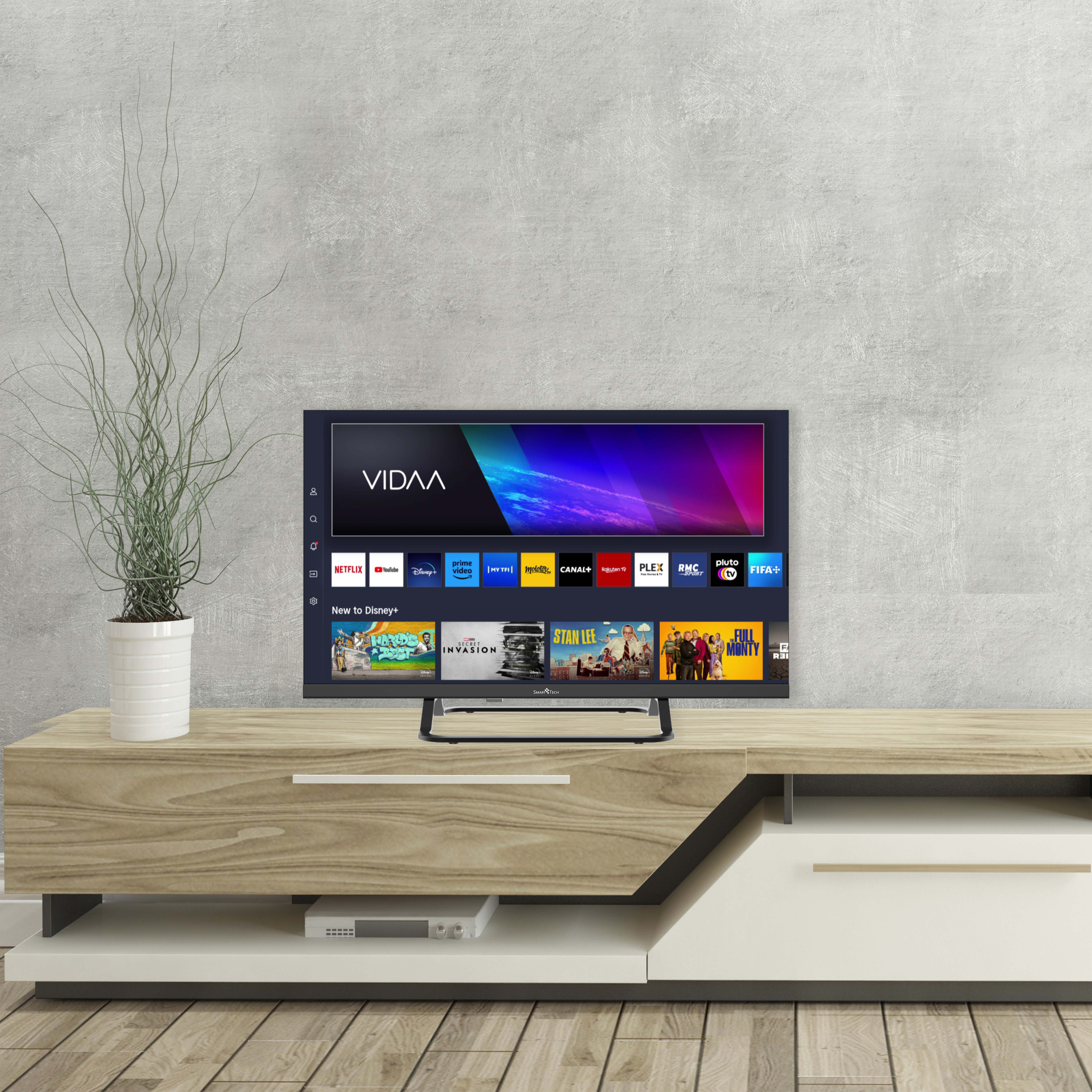 Telewizor na drewnianym stojaku. Ekran wyświetla interfejs VIDAA z ikonami aplikacji.