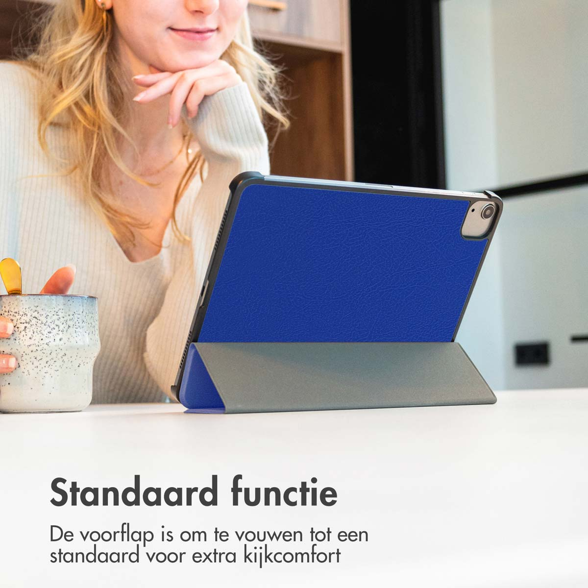 Une femme aux cheveux blonds utilise une tablette bleue. La tablette est sur une table, et le fond est flou.