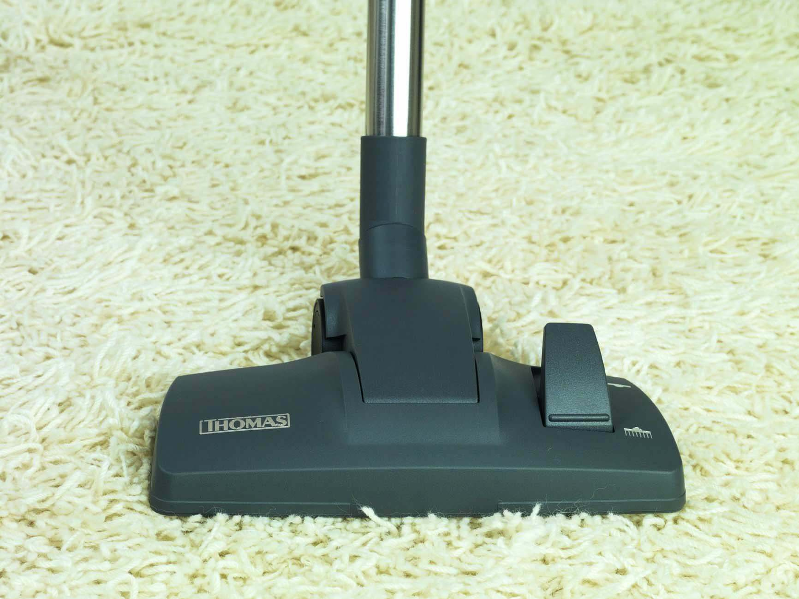Głowica odkurzacza znajduje się na puszystym białym dywanie, pod kątem, aby pokazać markę THOMAS.