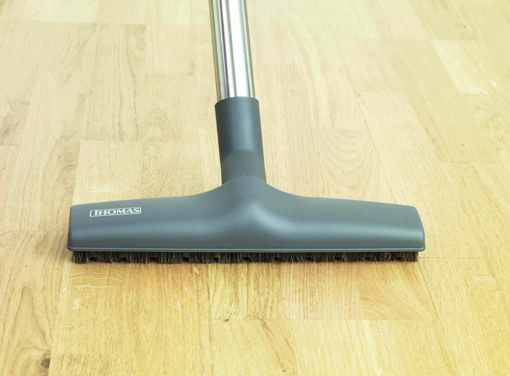 Głowica odkurzacza na drewnianej podłodze, pokazująca szczotkę i metalową rurę.