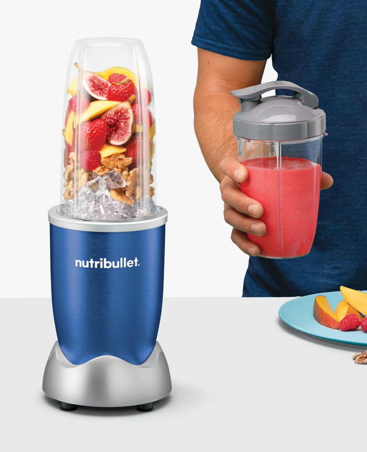 Frullatore con frutta e noci, e un frullato in una tazza. Una persona tiene in mano la tazza.