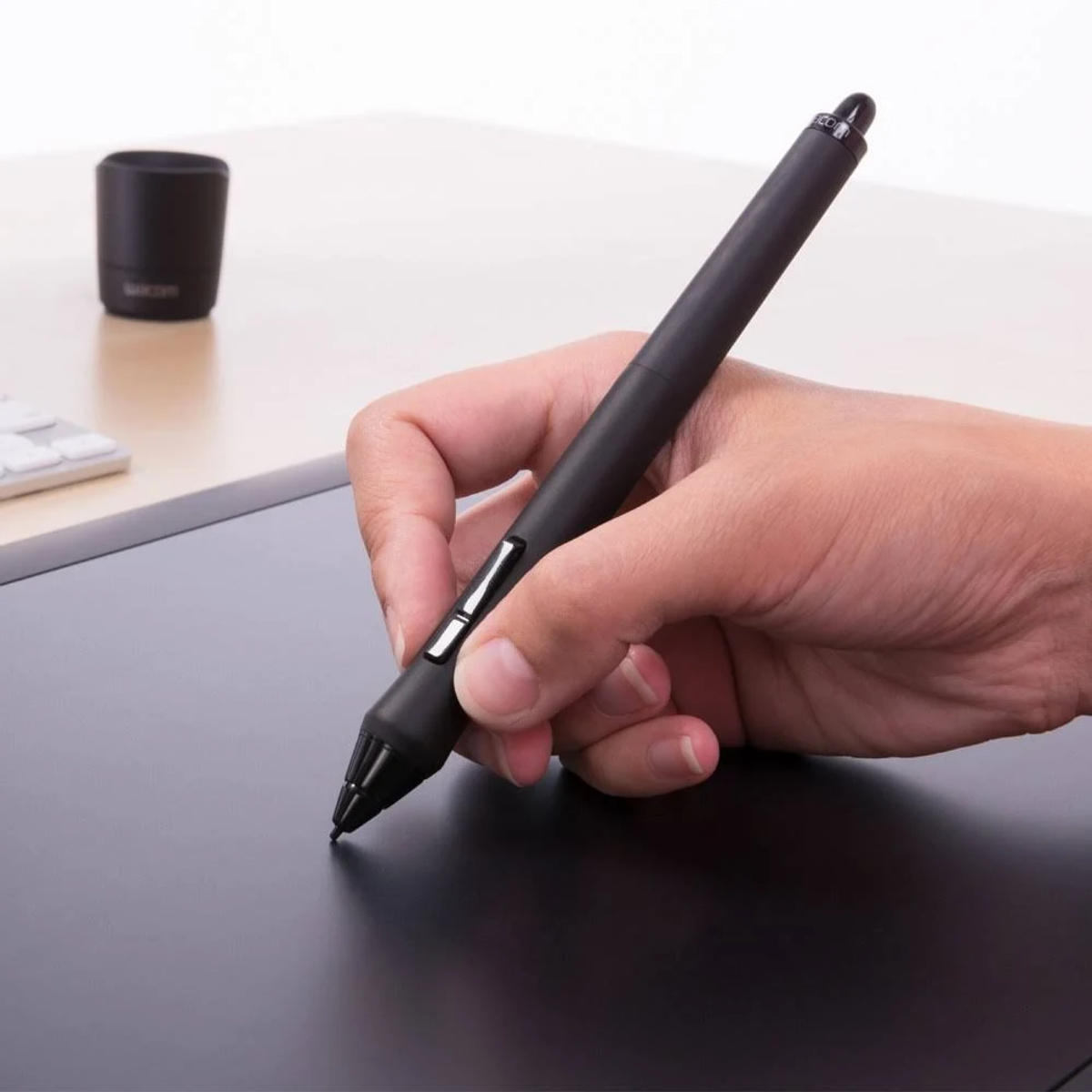 Una mano tiene una penna nera sopra un tablet nero, su una superficie chiara.