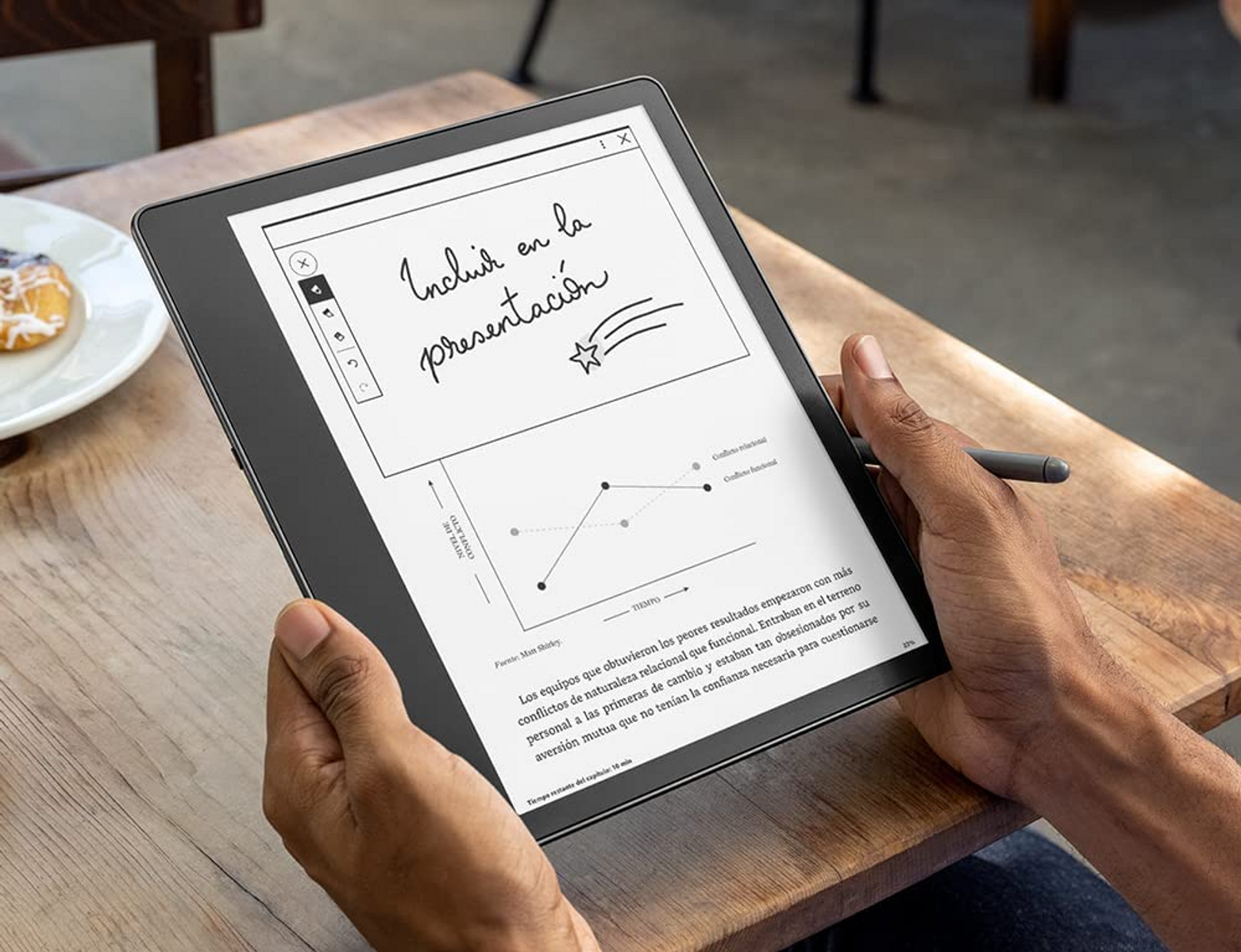 Osoba trzymająca tablet z cyfrową notatką i wykresem na drewnianym stole.