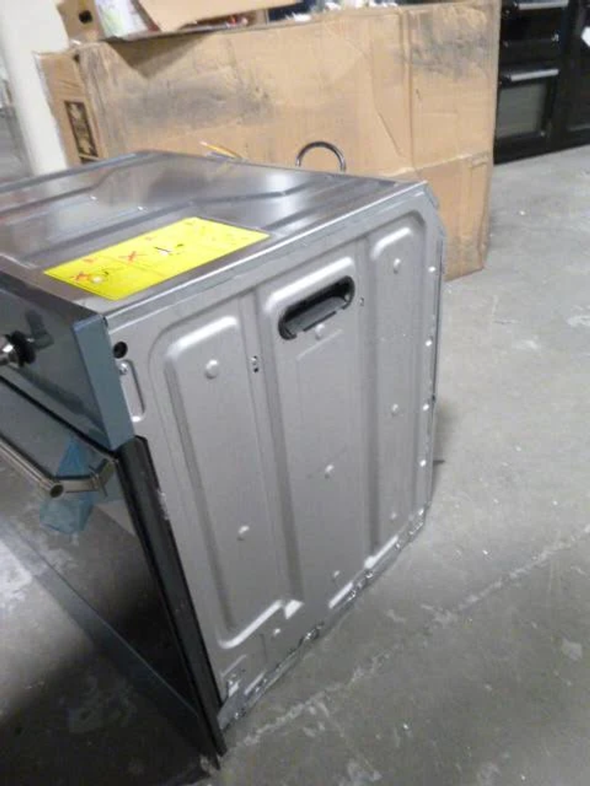 Un horno plateado, parcialmente fuera de una caja de cartón en un suelo de concreto.