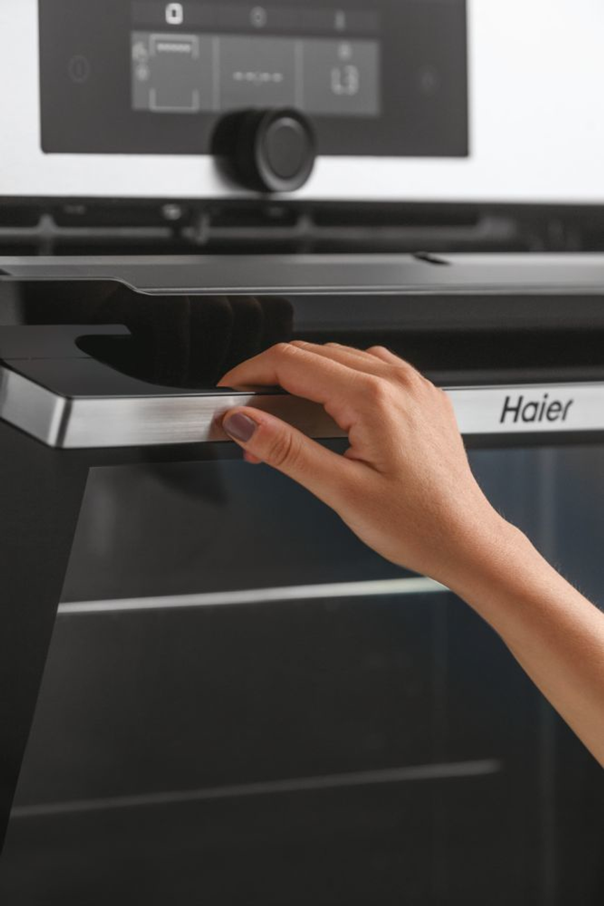 Una mano apre la porta di un forno nero, con il marchio Haier visibile.