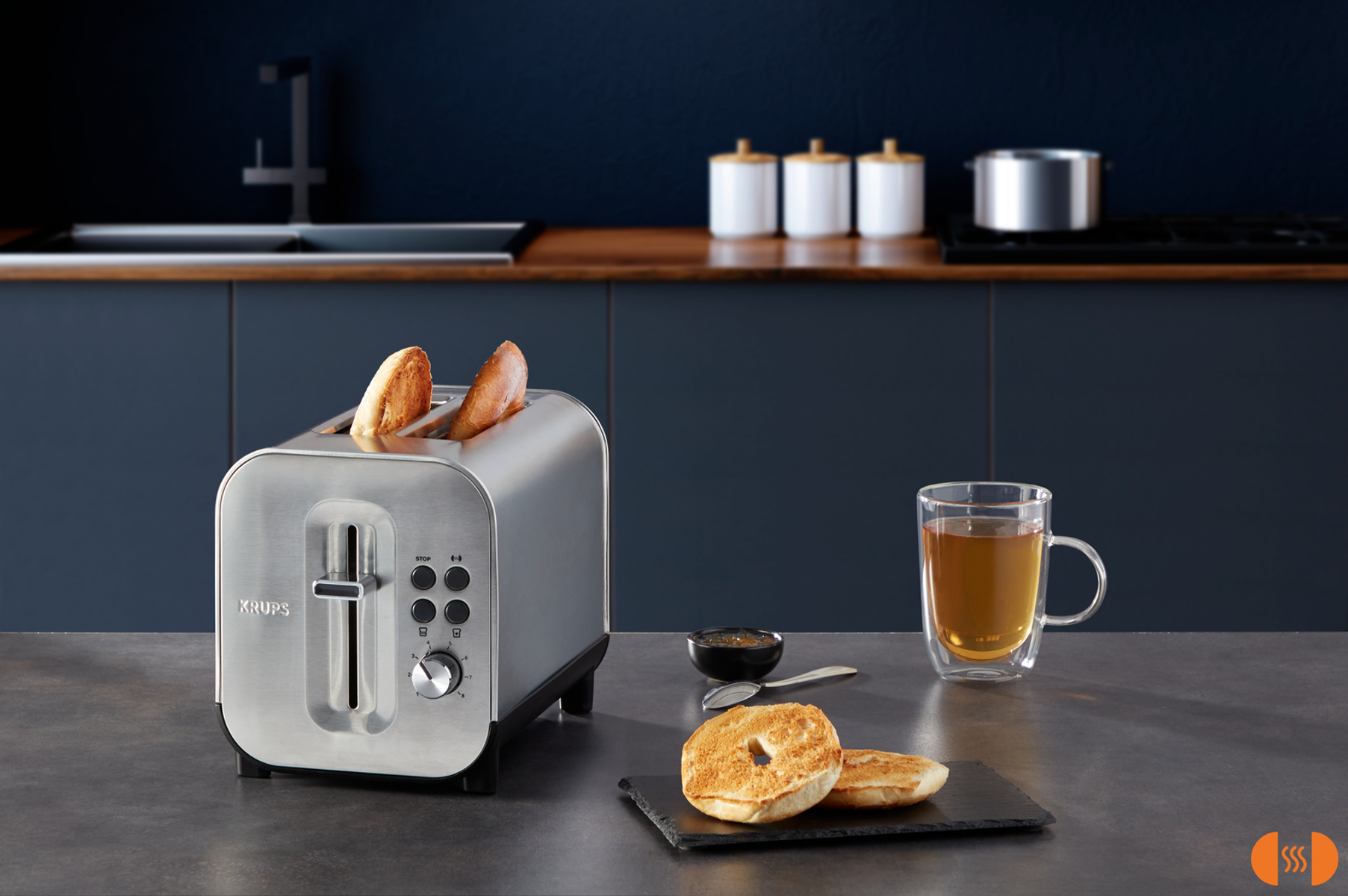 Srebrny toster z kromkami chleba, filiżanka herbaty i bajgle na stole.