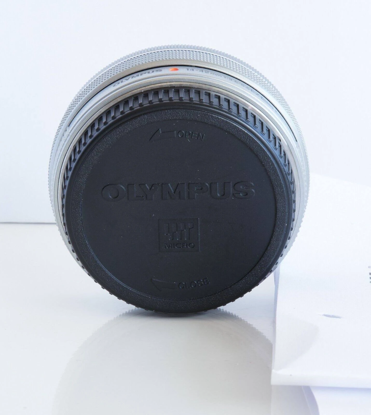 Een Olympus cameralens met de dop erop, met de merknaam en de details van de lens.