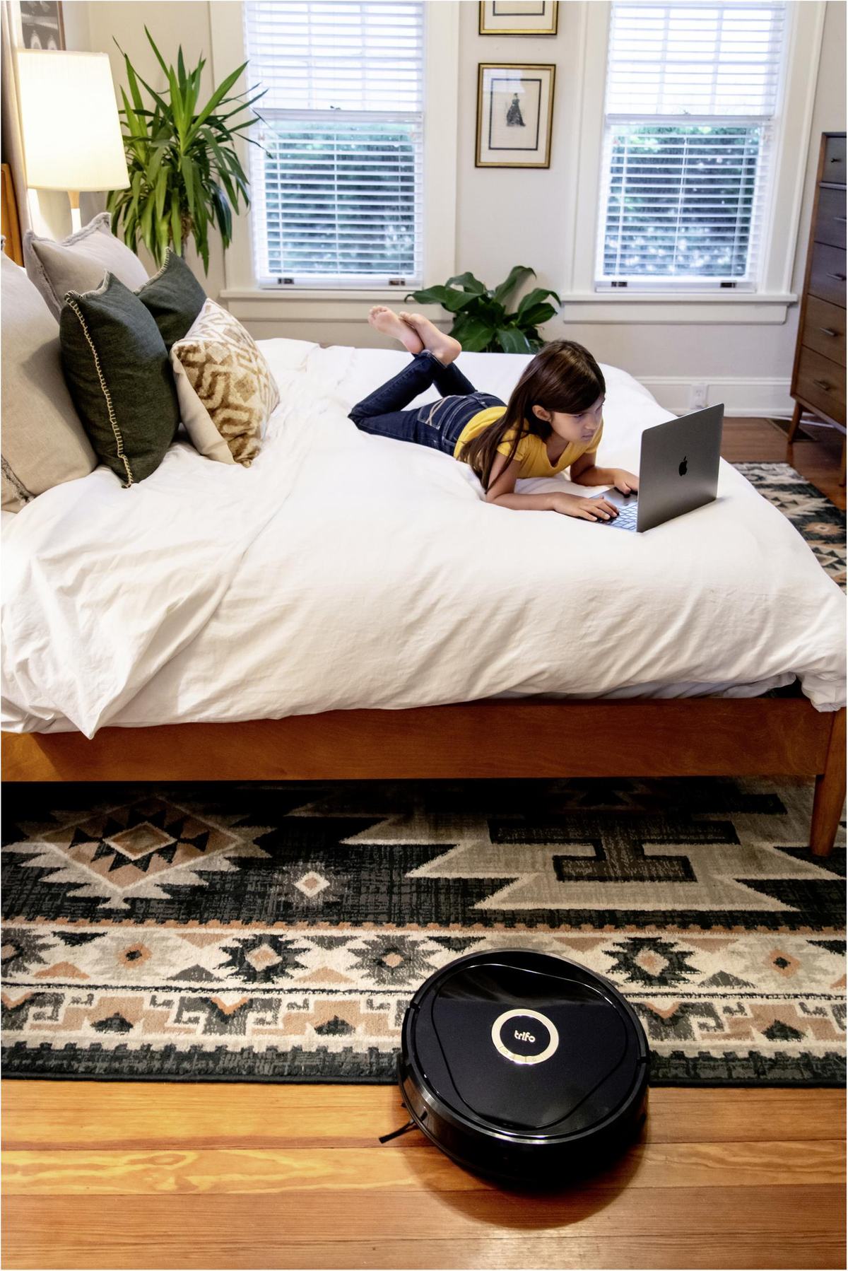 Dziewczyna używa laptopa na łóżku. Robot sprzątający jest na podłodze.
