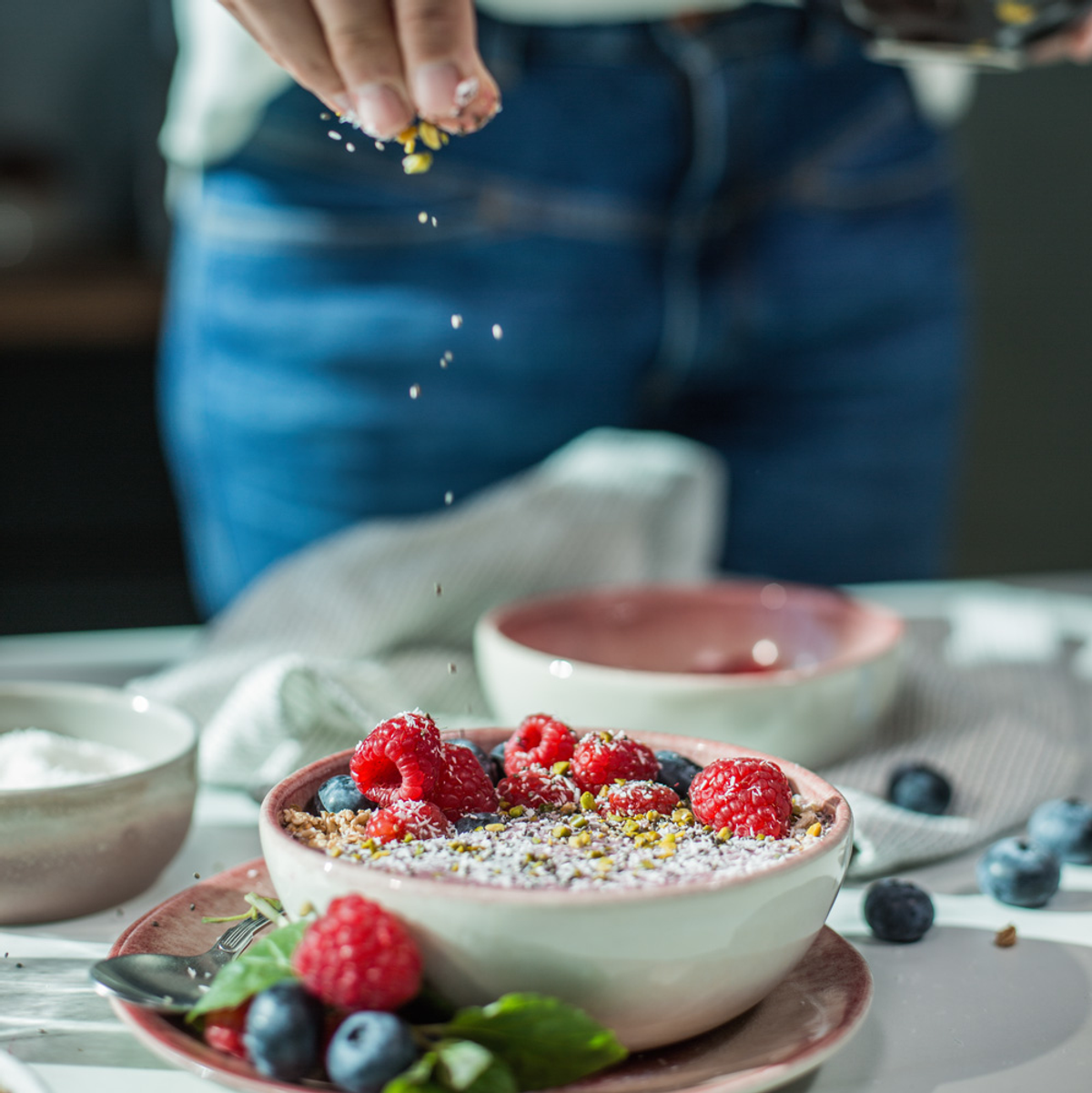 Eine Person bestreut eine Schüssel Haferflocken mit Beeren, weitere Beeren liegen daneben.
