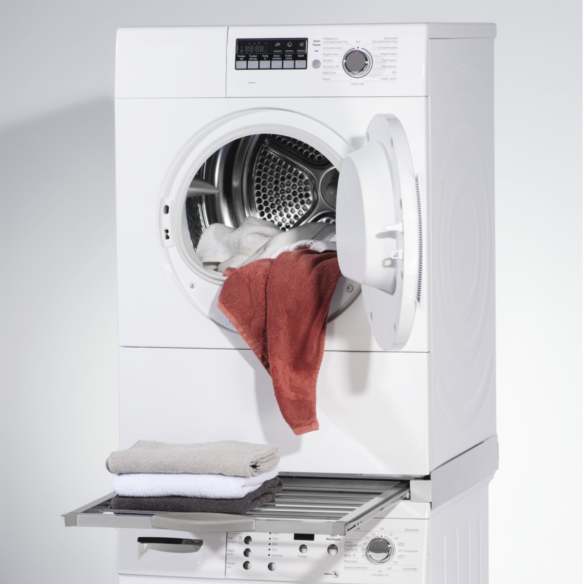 Eine Waschmaschine mit offener Tür, Kleidung und ein Trockengestell sichtbar.