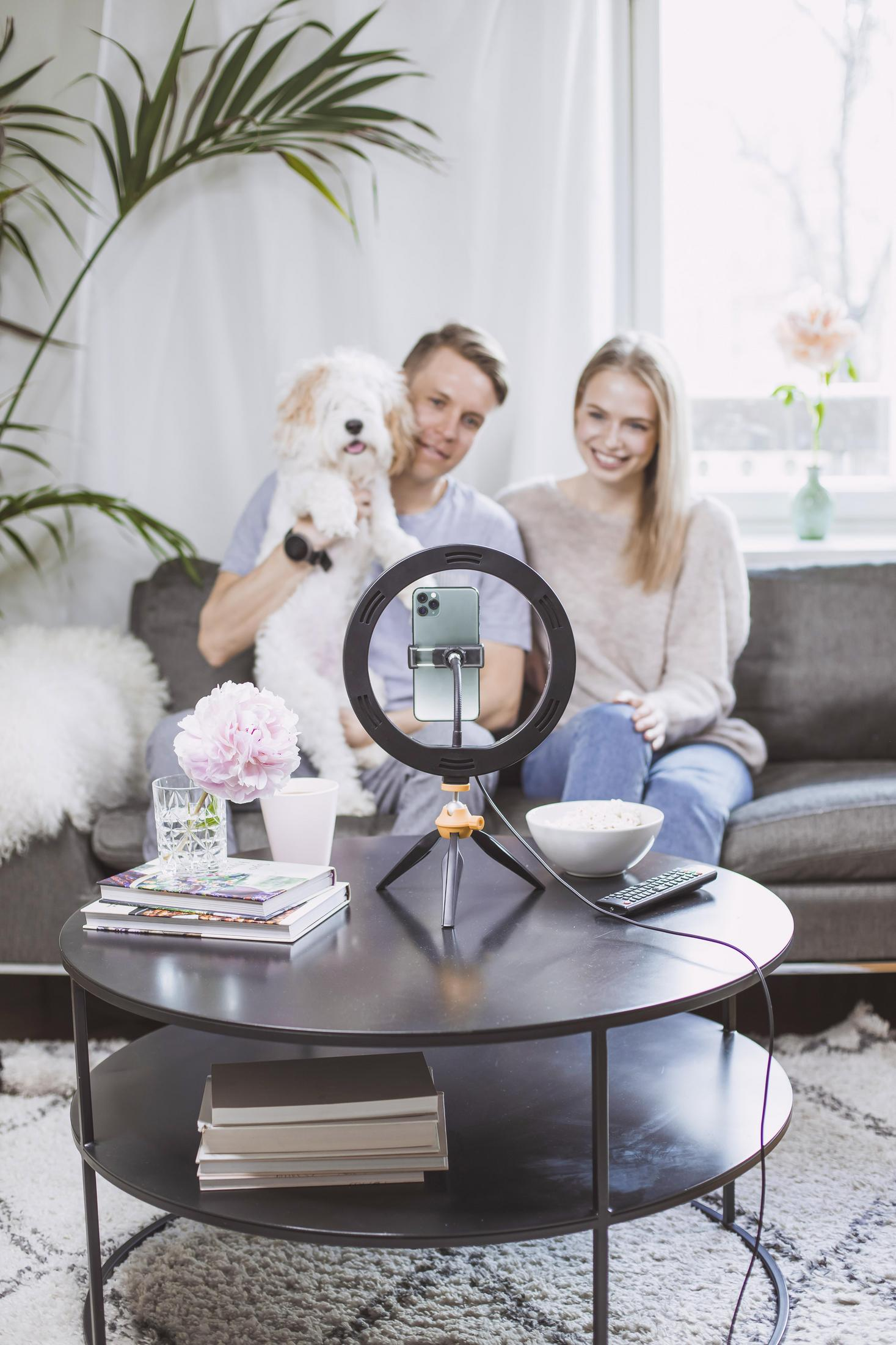 Una coppia con un cane e una ring light che filma. C'è un tavolino con oggetti.