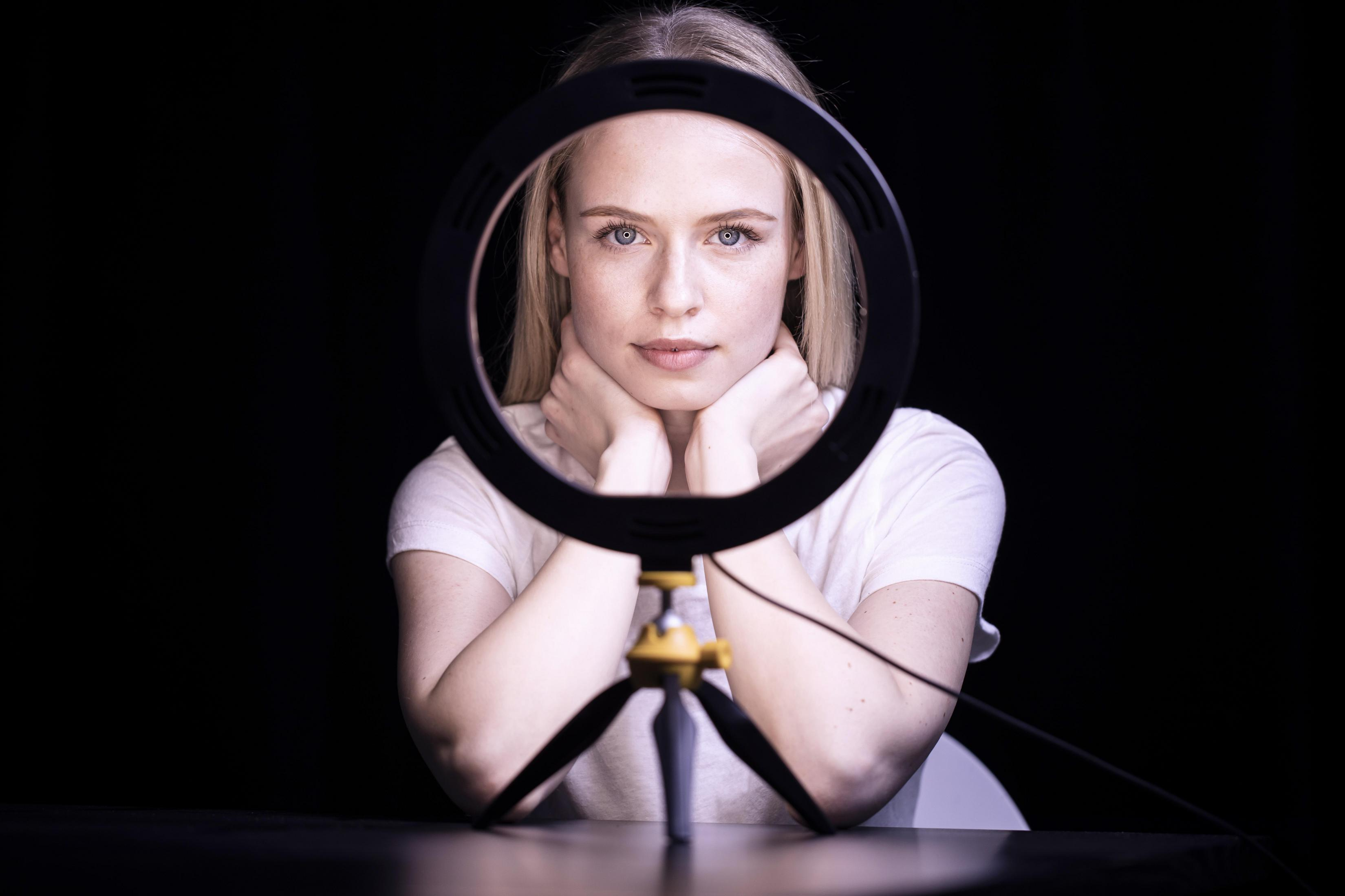 Una donna che guarda attraverso una ring light su sfondo nero.