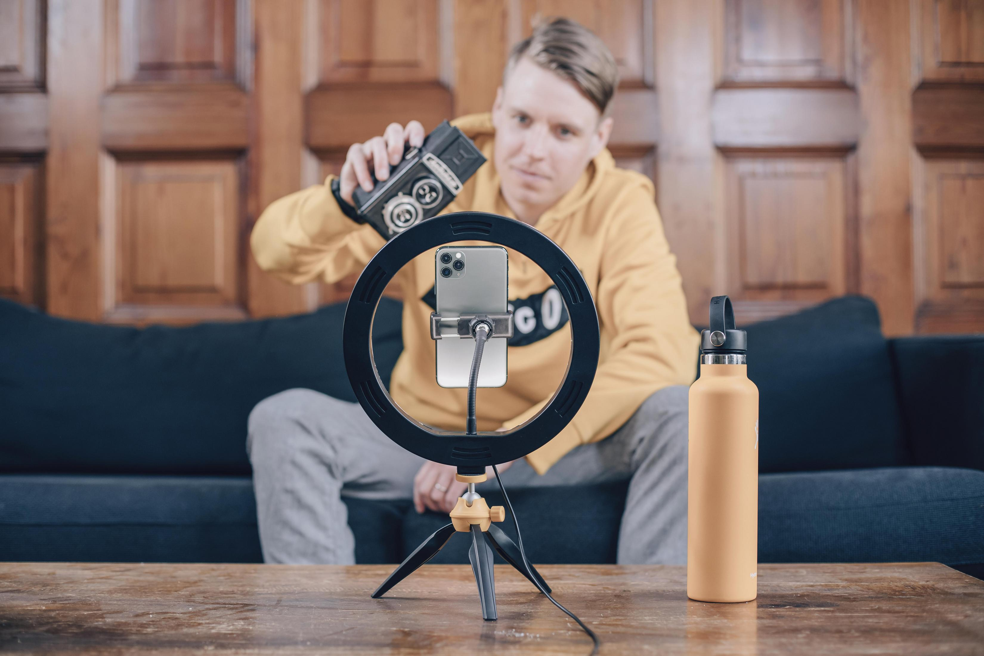 Una persona che configura un anello luminoso e un telefono su un treppiede per un video.