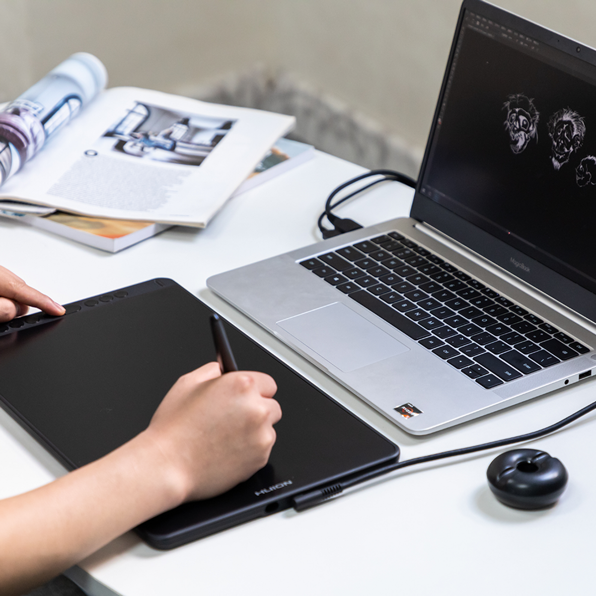 A person using a digital drawing tablet and a laptop on a white desk.