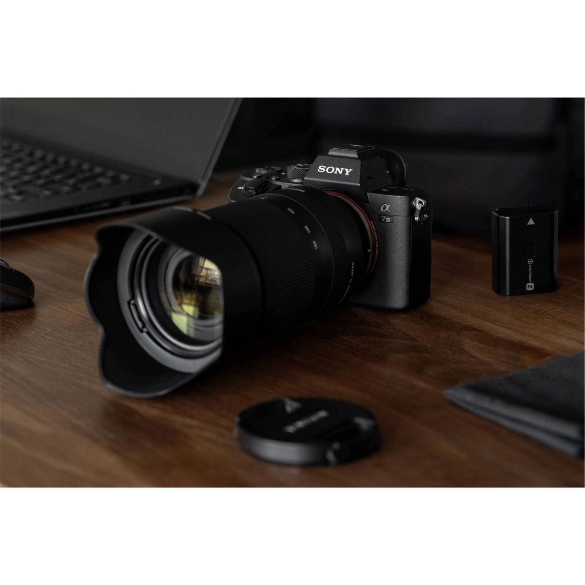 Czarny aparat Sony z obiektywem na drewnianym stole z baterią i osłoną obiektywu.