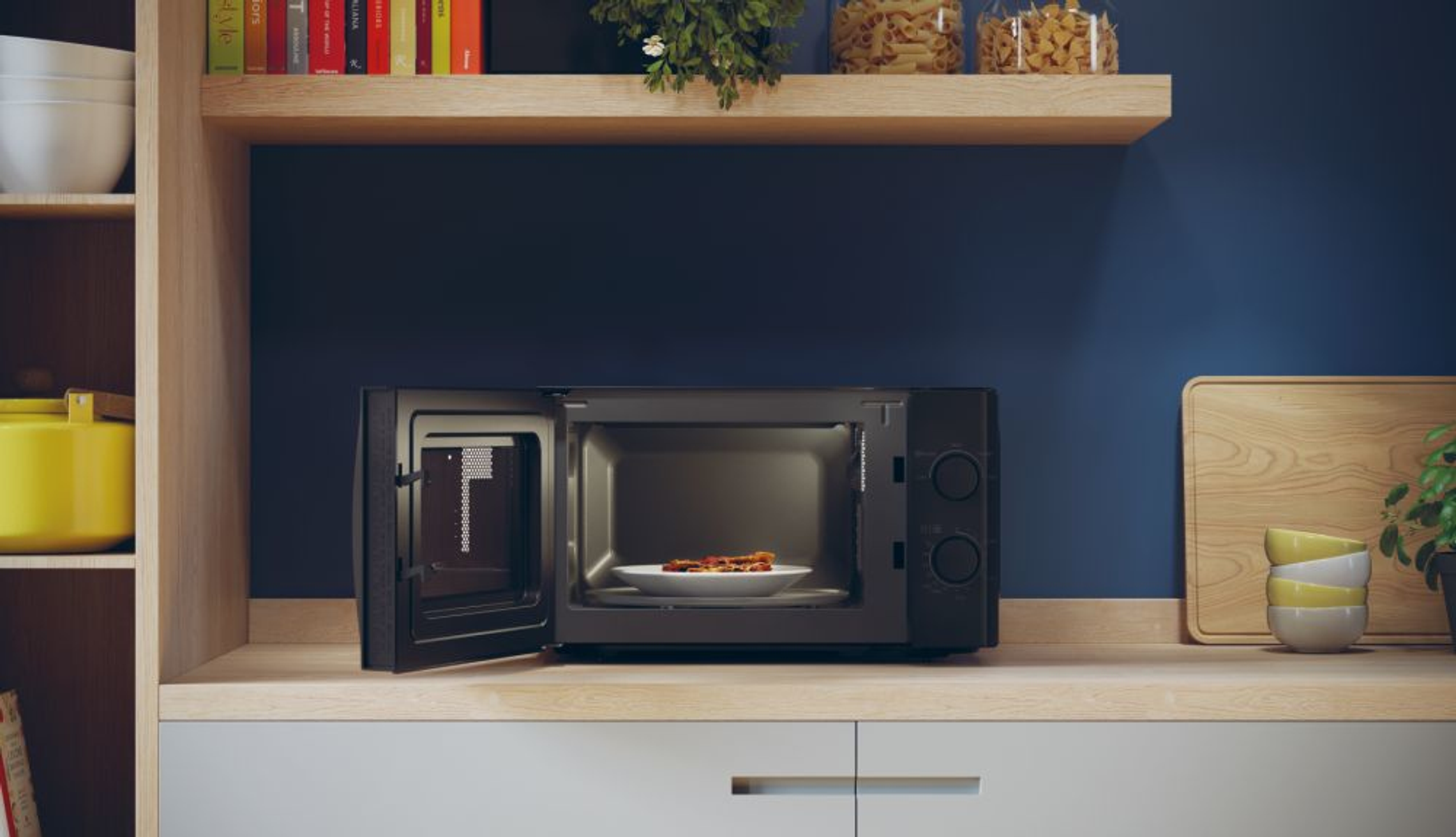 Czarna kuchenka mikrofalowa z otwartymi drzwiami, talerz z jedzeniem w środku, na drewnianym blacie. Niebieska ściana w tle.