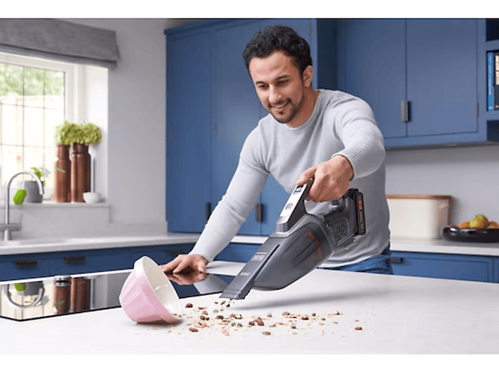 Un hombre aspira una encimera de cocina, hay un cuenco y migas.