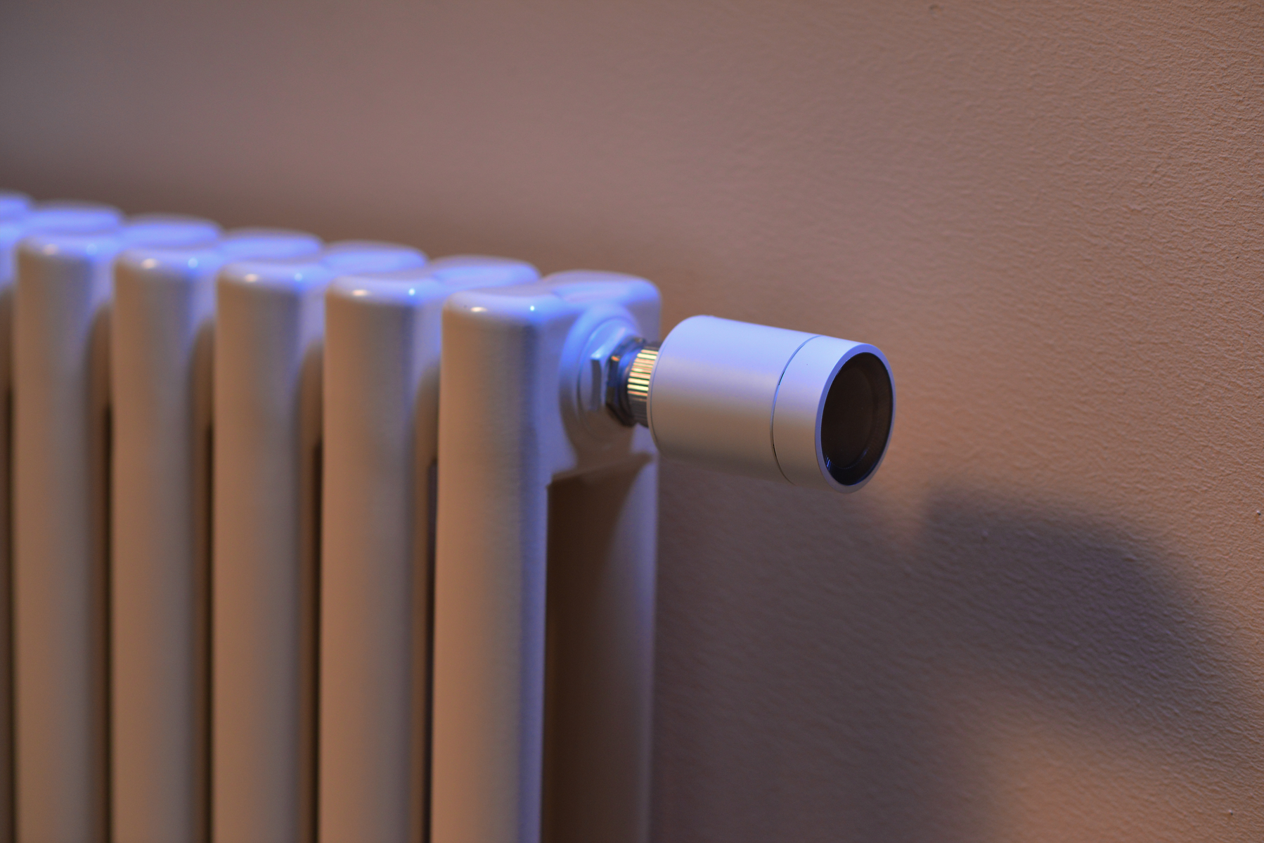 Ein weißer Heizkörper mit einem modernen Thermostat. Er steht an einer beigen Wand und das Thermostat ist weiß und grau.