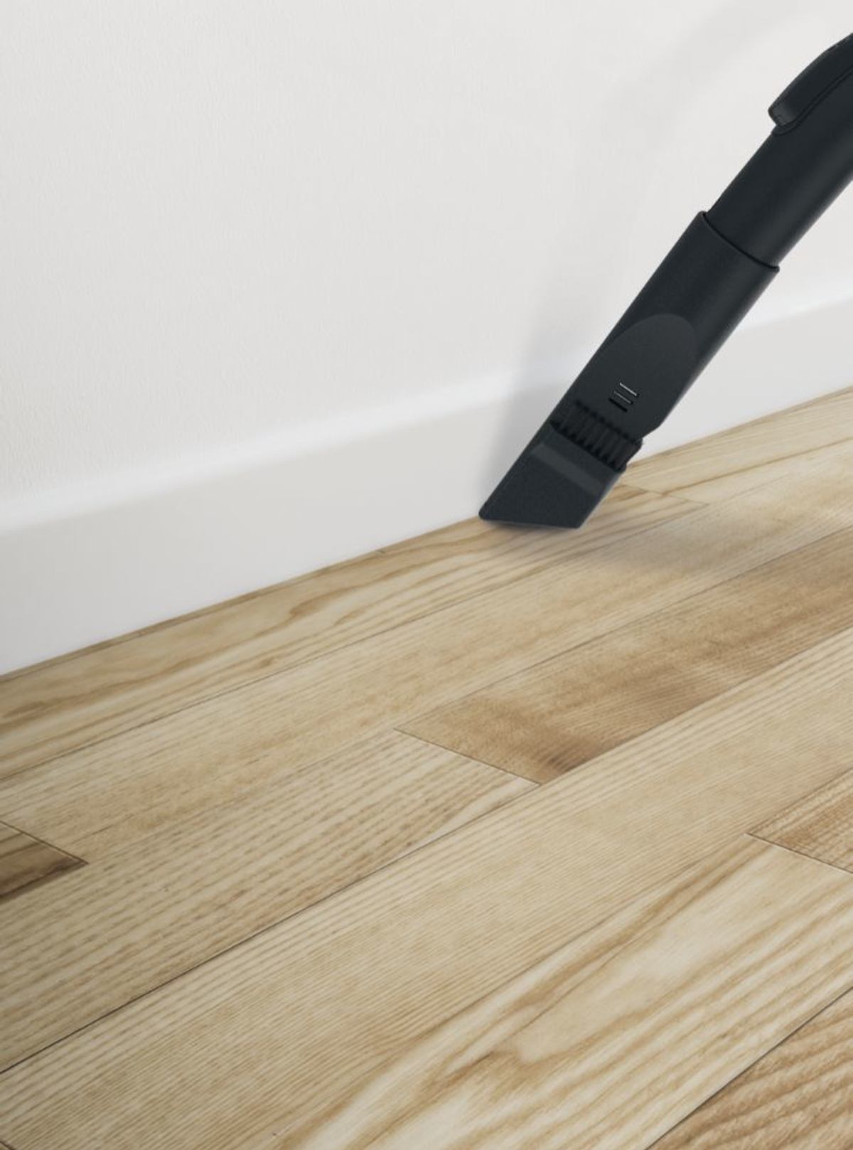Testa aspirapolvere nera pulisce pavimento in legno, muro bianco.