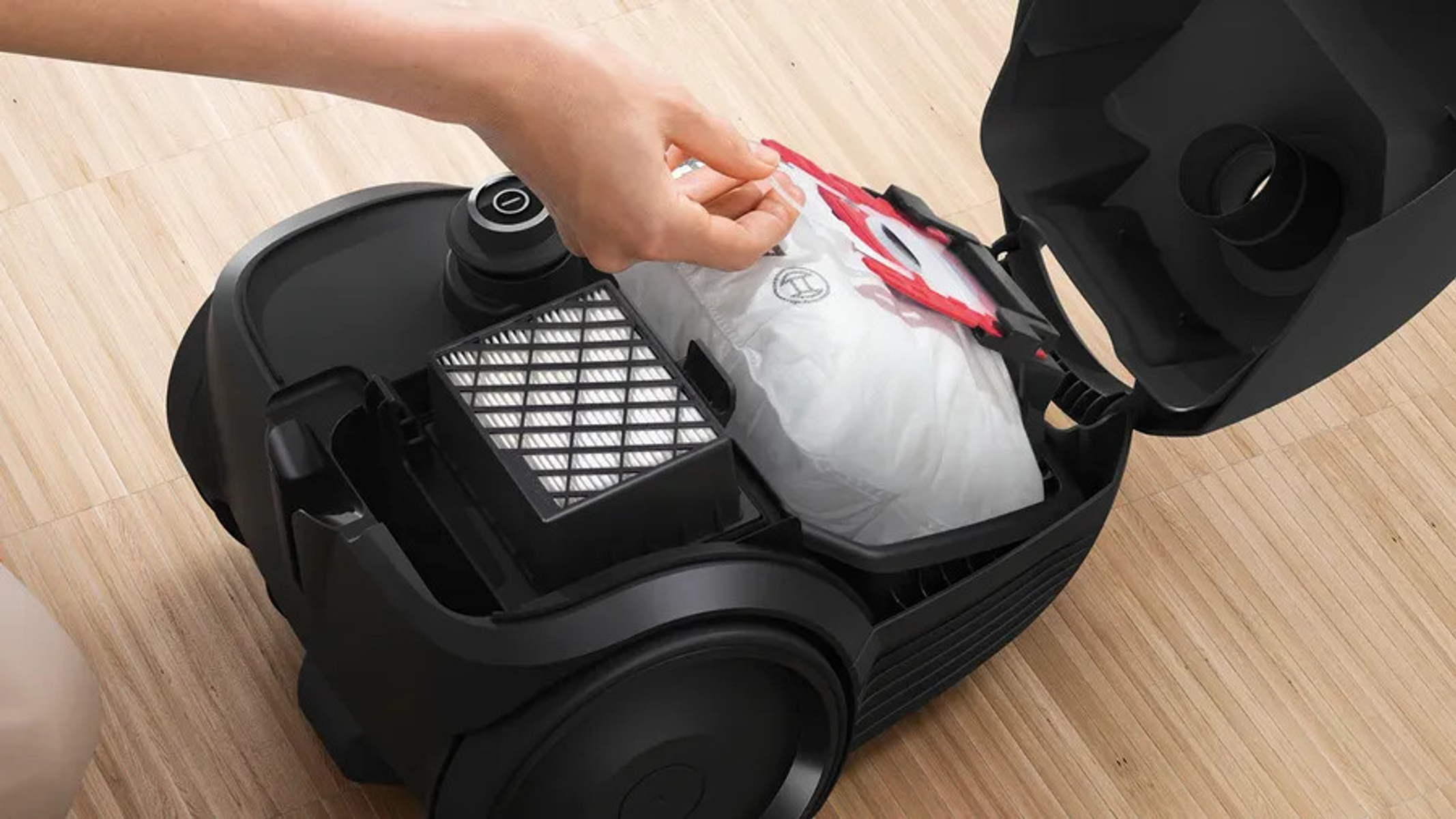 Osoba wyjmująca biały worek do odkurzacza z czarnego odkurzacza.