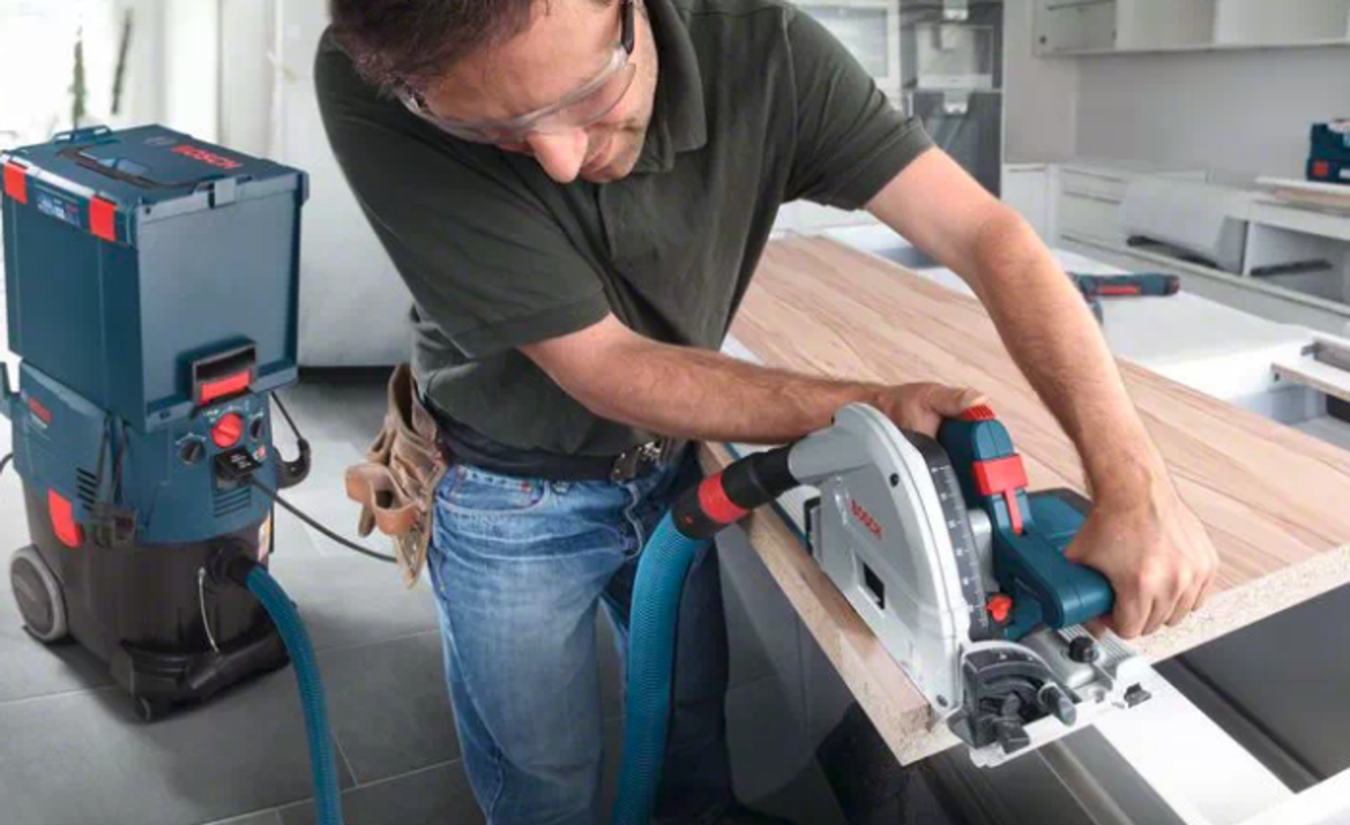 Hombre usando una sierra circular Bosch para cortar una tabla de madera con una aspiradora cerca.