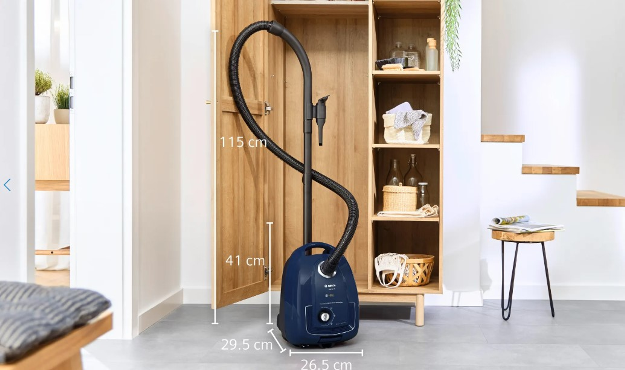 Niebieski odkurzacz Bosch z wymiarami, stojący w drewnianej szafce.