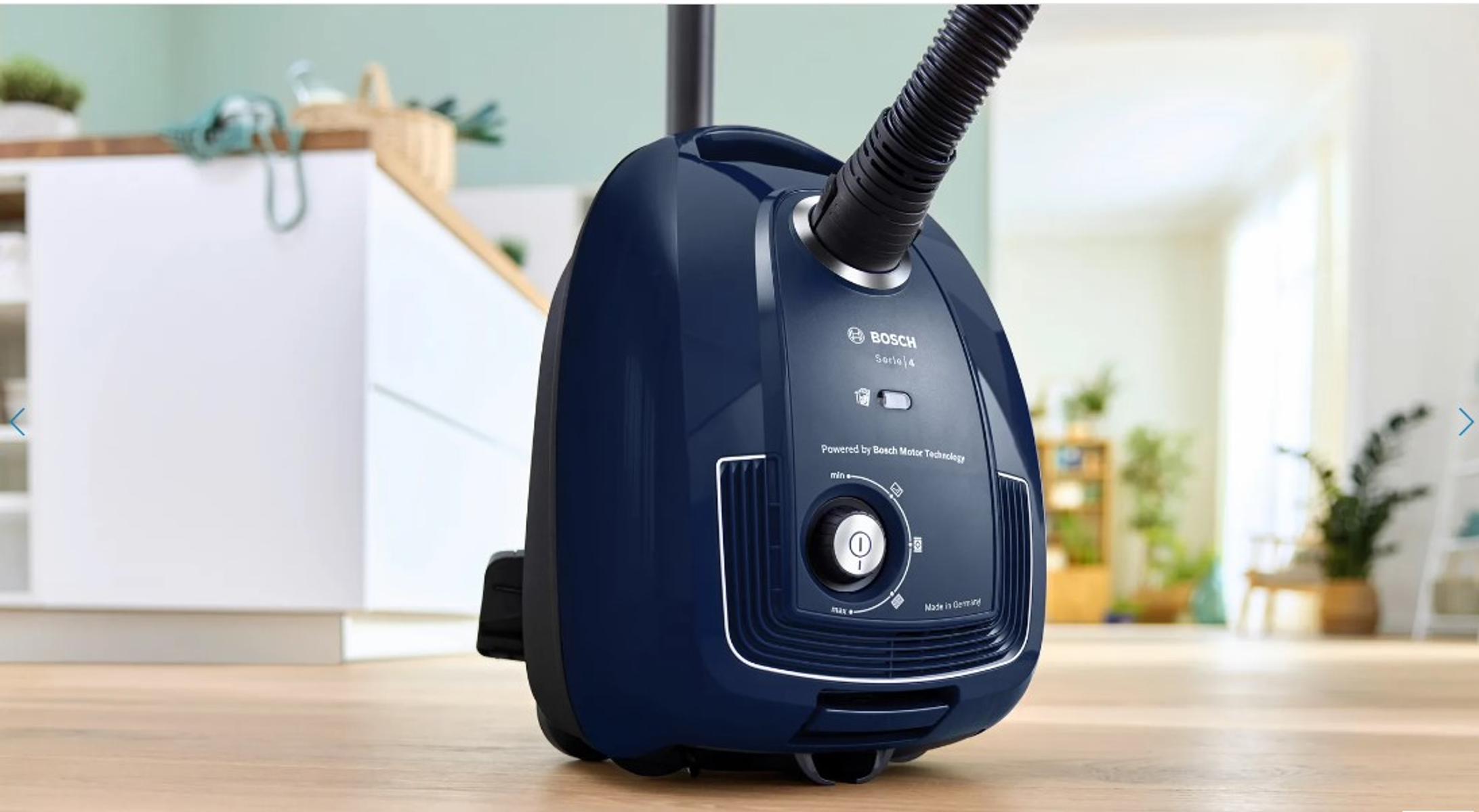 Granatowy odkurzacz Bosch na drewnianej podłodze w kuchni.