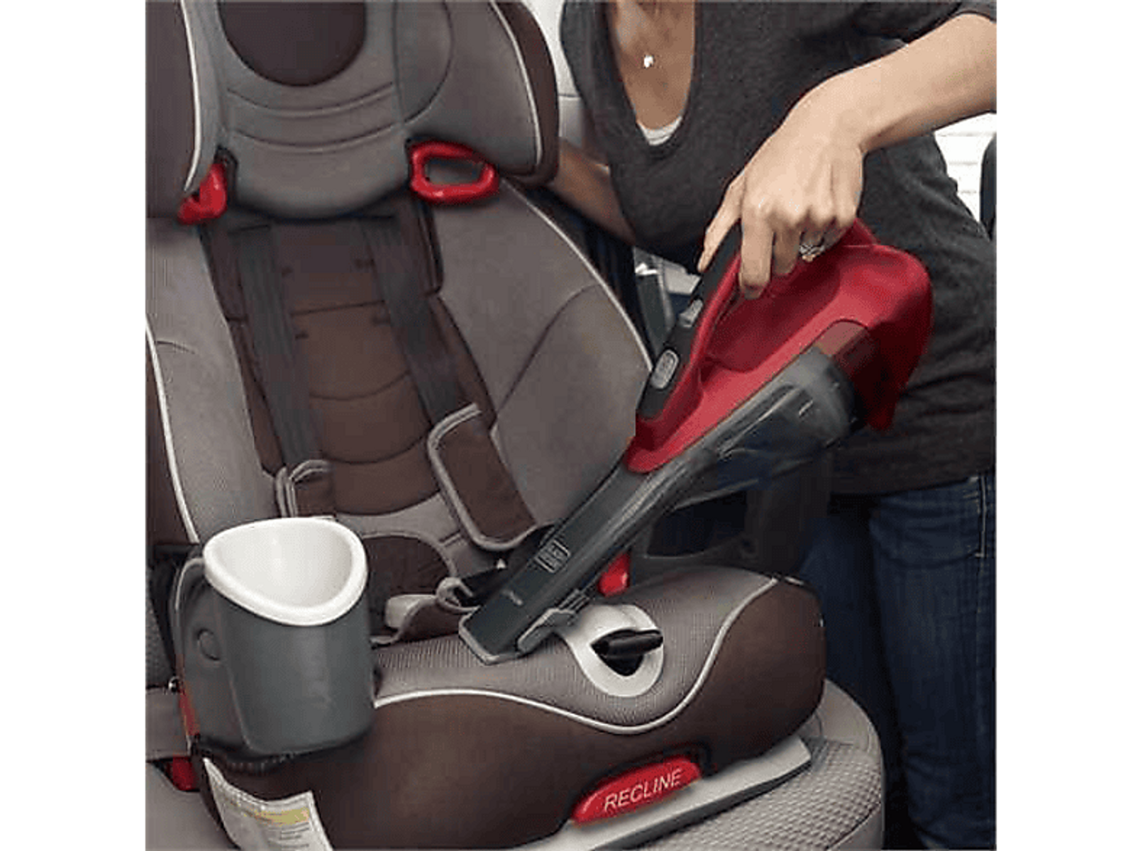 Una persona aspirando con una aspiradora de mano roja y negra en un asiento de coche.