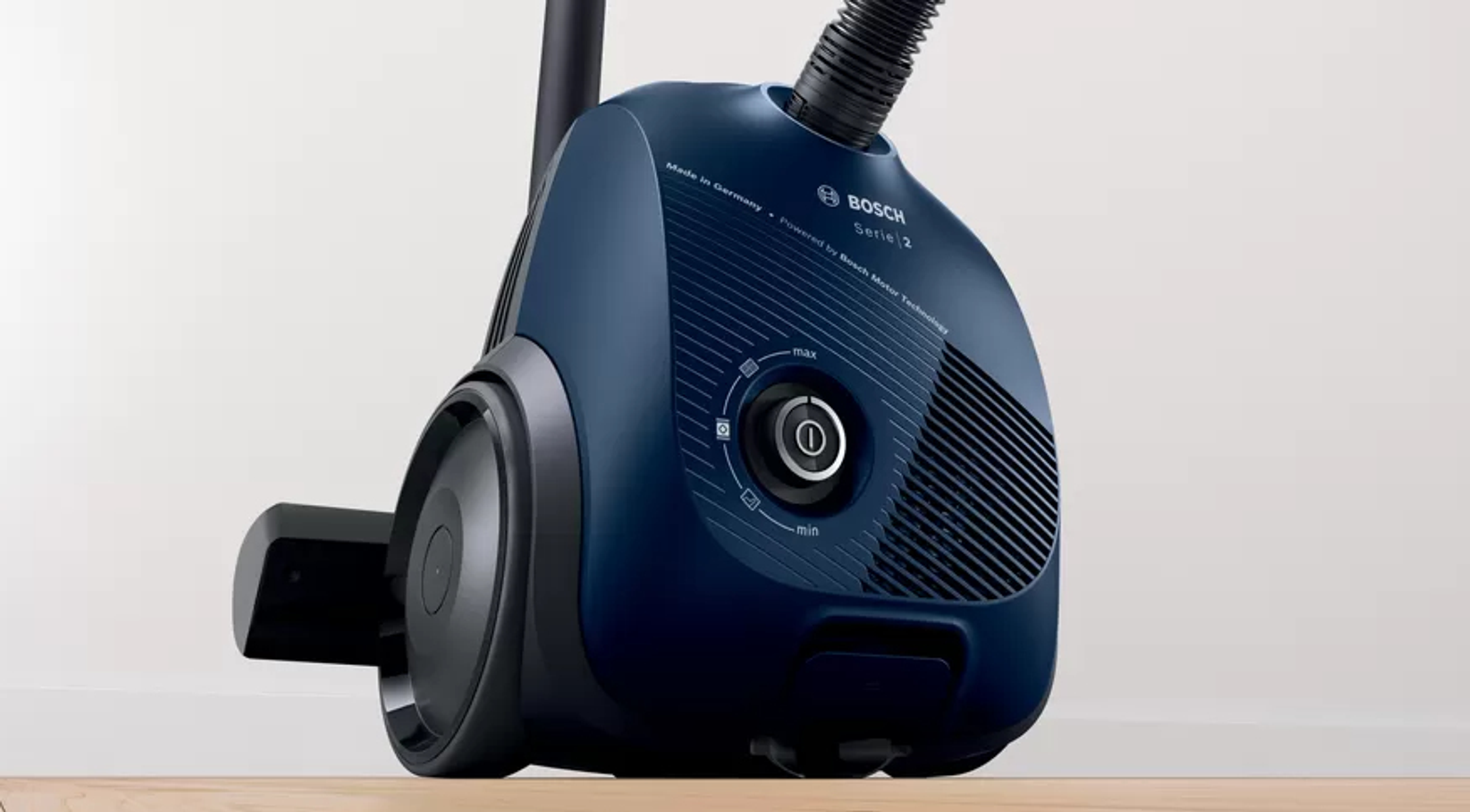 Zbliżenie ciemnoniebieskiego odkurzacza Bosch. Odkurzacz stoi na drewnianej powierzchni.