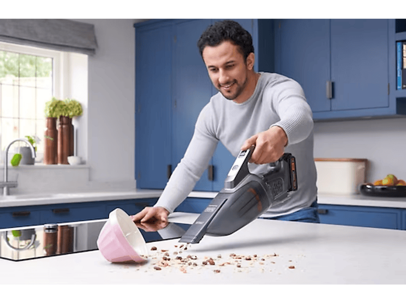 Mann mit Staubsauger. Krümel liegen auf der weißen Arbeitsplatte und rosa Schüssel.