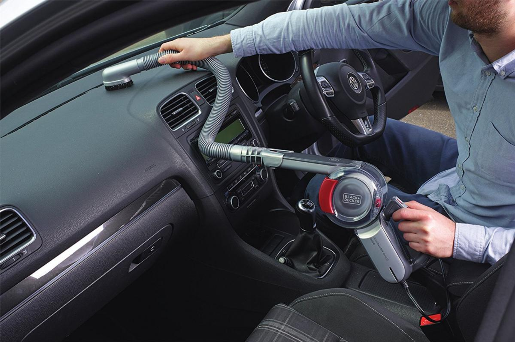 Une personne utilisant un aspirateur dans une voiture. L'aspirateur nettoie le tableau de bord.