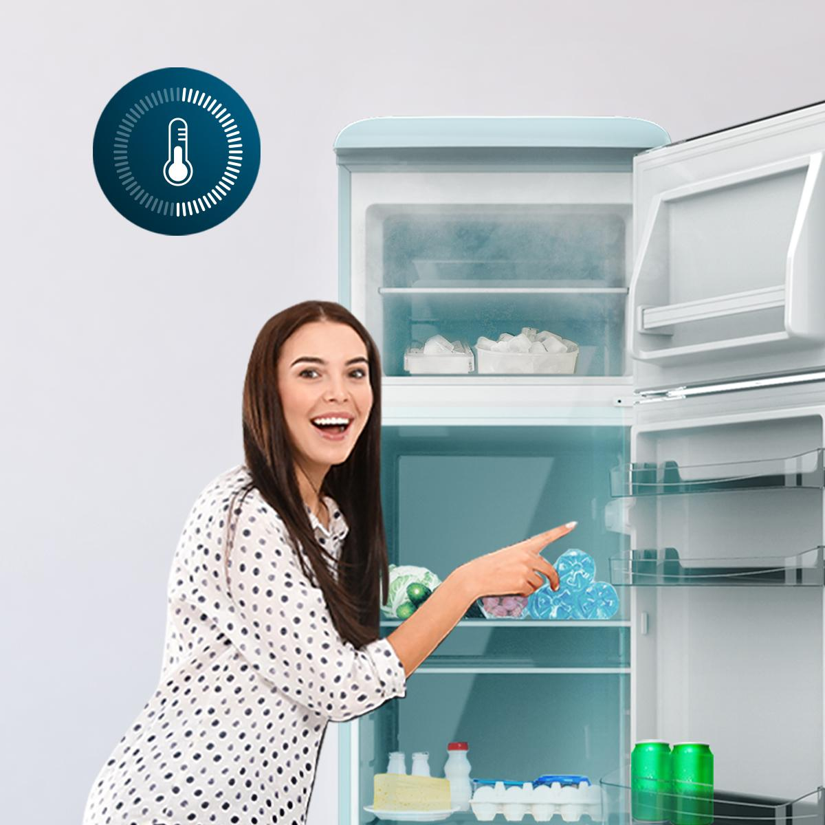 Una mujer sonríe, señalando una nevera. La nevera está abierta, mostrando estantes con comida.