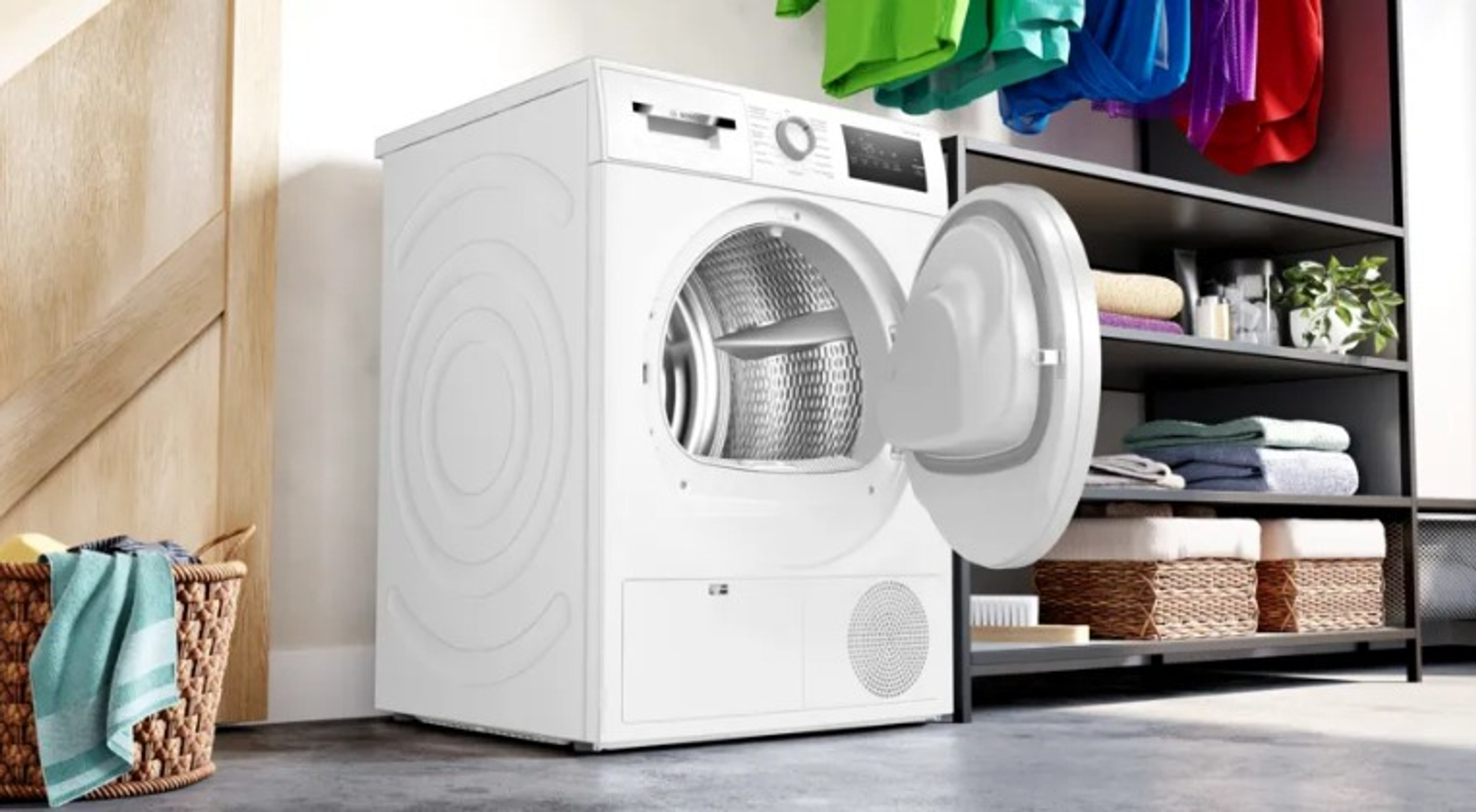Un lave-linge blanc avec une porte ouverte et un sèche-linge derrière. Un panier à linge devant.
