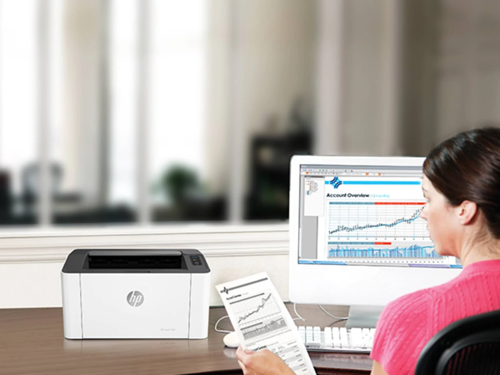 Una donna guarda lo schermo di un computer con un grafico, una stampante è sulla scrivania di fronte a lei.