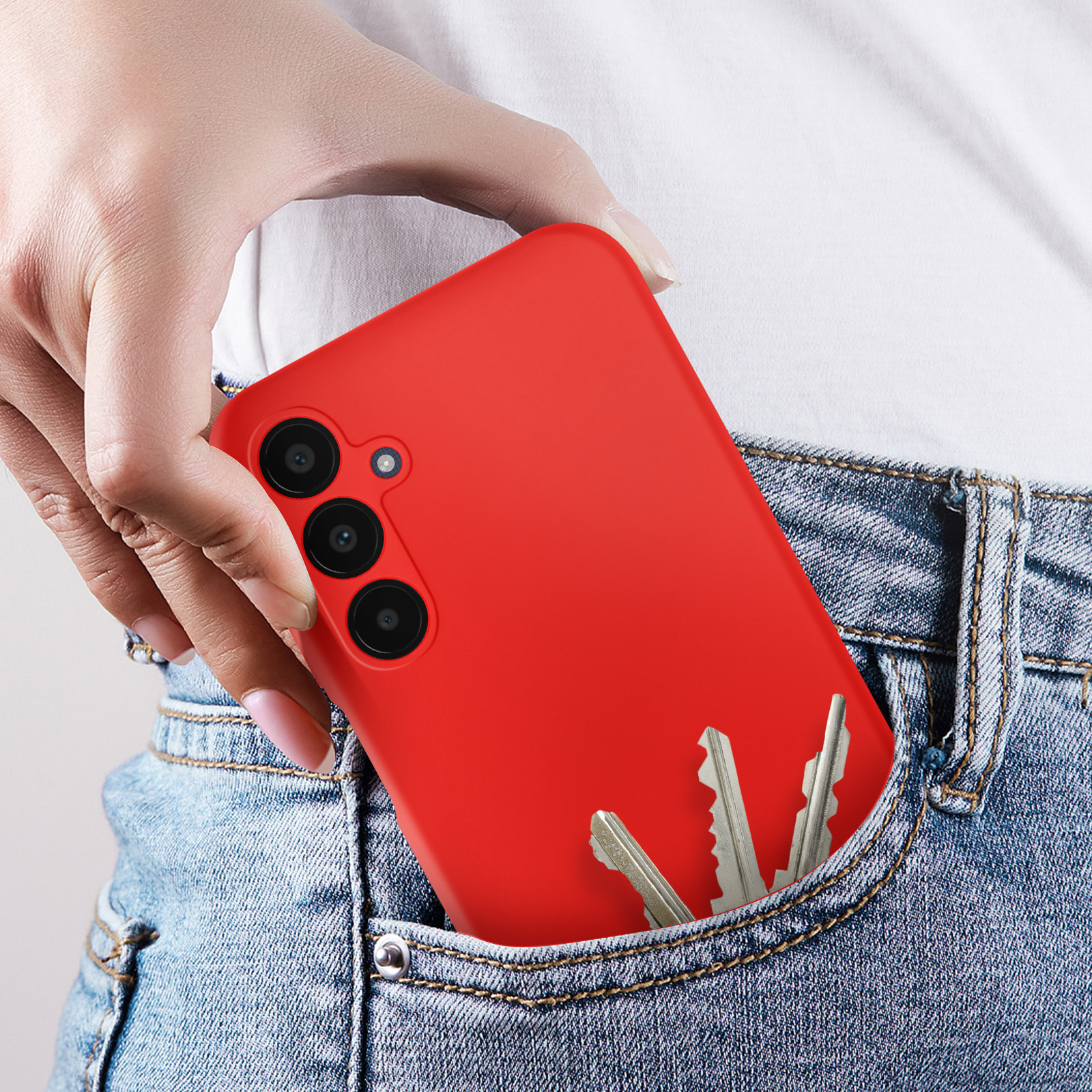 La mano di una persona nella tasca dei jeans che tiene una custodia rossa per telefono e delle chiavi.