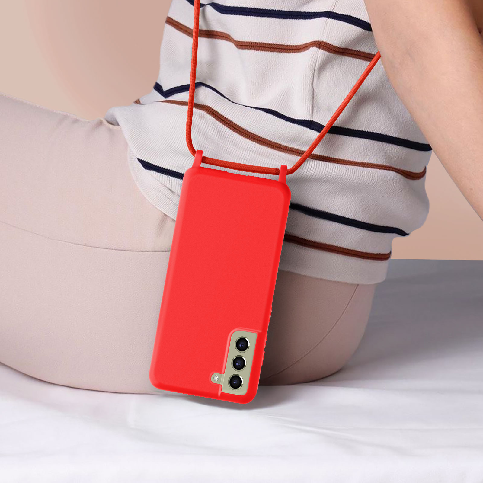 Una custodia per telefono rossa con un cordino. Una persona è seduta con il telefono davanti.