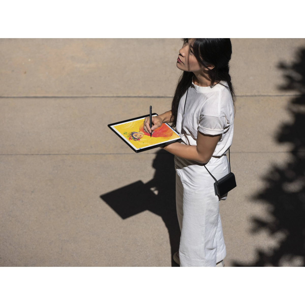 Kobieta w bieli rysuje na tablecie na zewnątrz, widoczne światło słoneczne i cienie.