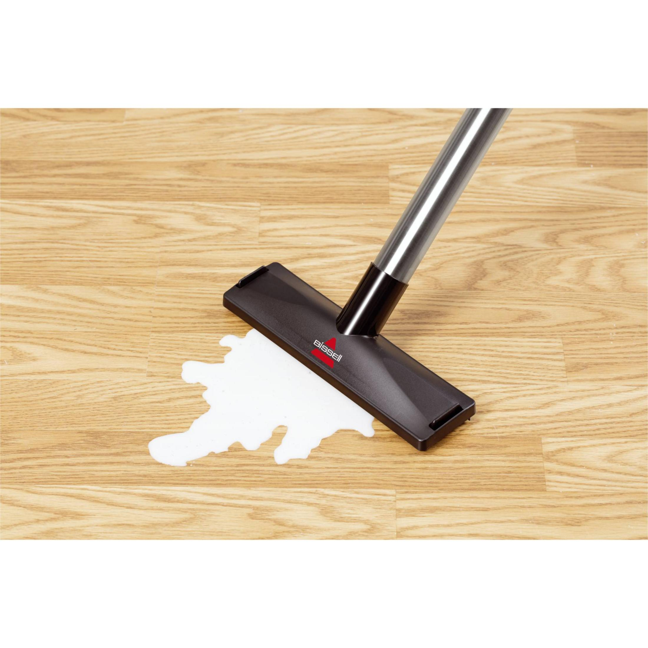 Testa di aspirapolvere su pavimento in legno con liquido. Il logo Bissell è visibile sull'aspirapolvere.