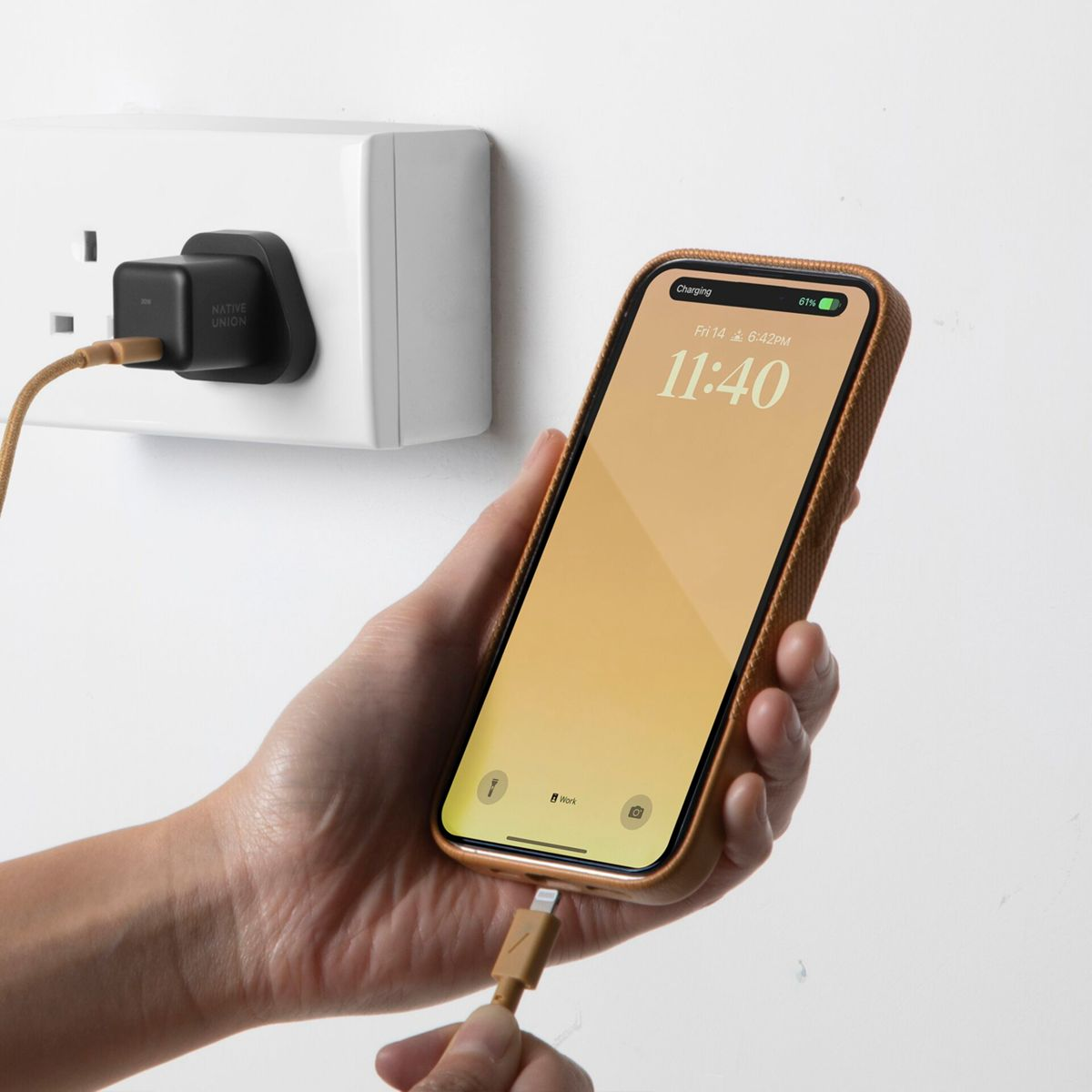 Mano che tiene un telefono in carica con una spina nel muro.