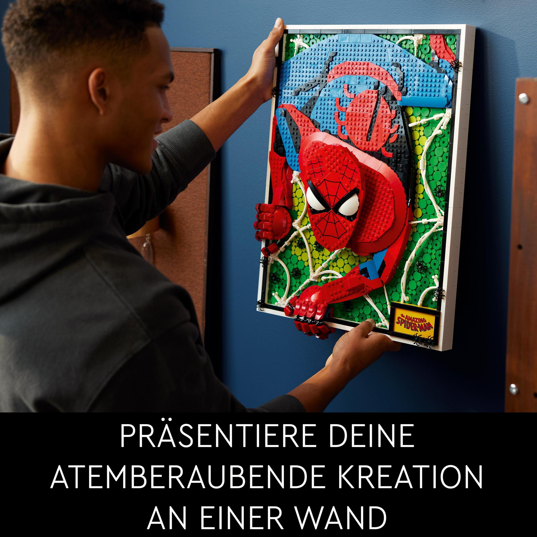 Mężczyzna trzymający na ścianie dzieło sztuki Lego Spider-Man.