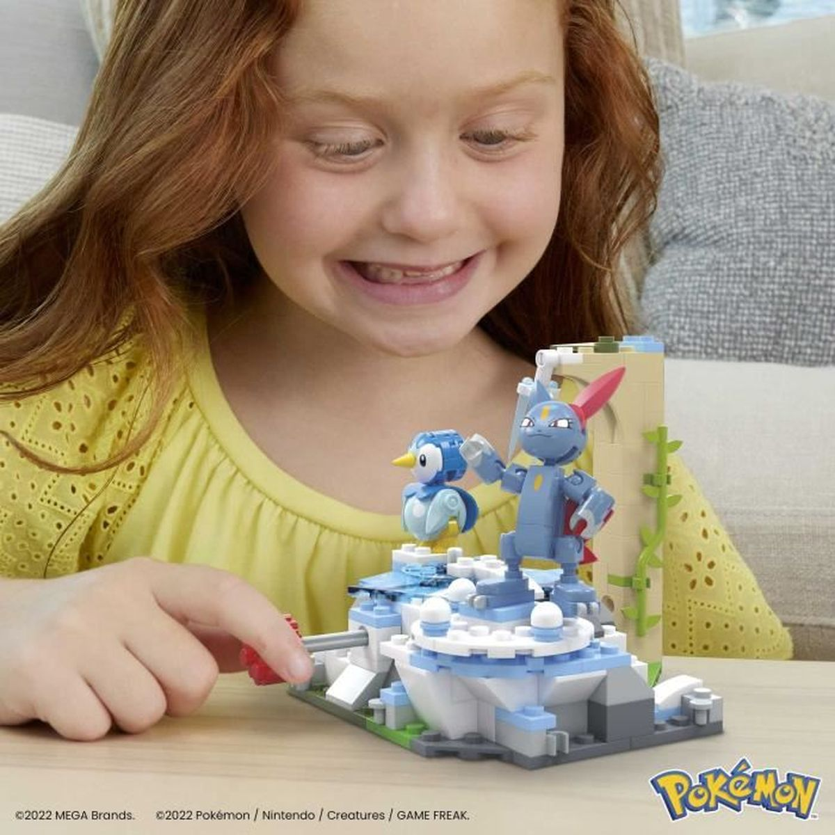 Una ragazza sorride a un set di giocattoli Pokemon. Figure blu e grigie su una struttura Lego.