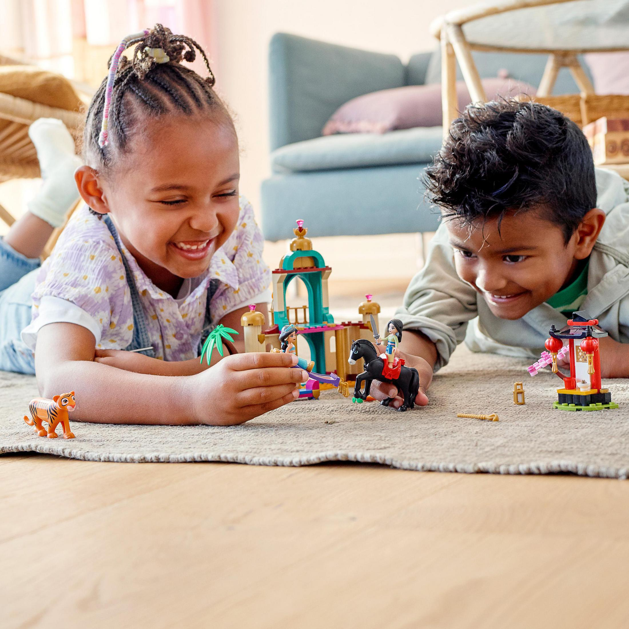 Due bambini che giocano con i Lego su un tappeto. Un edificio e delle figurine sono di fronte a loro.