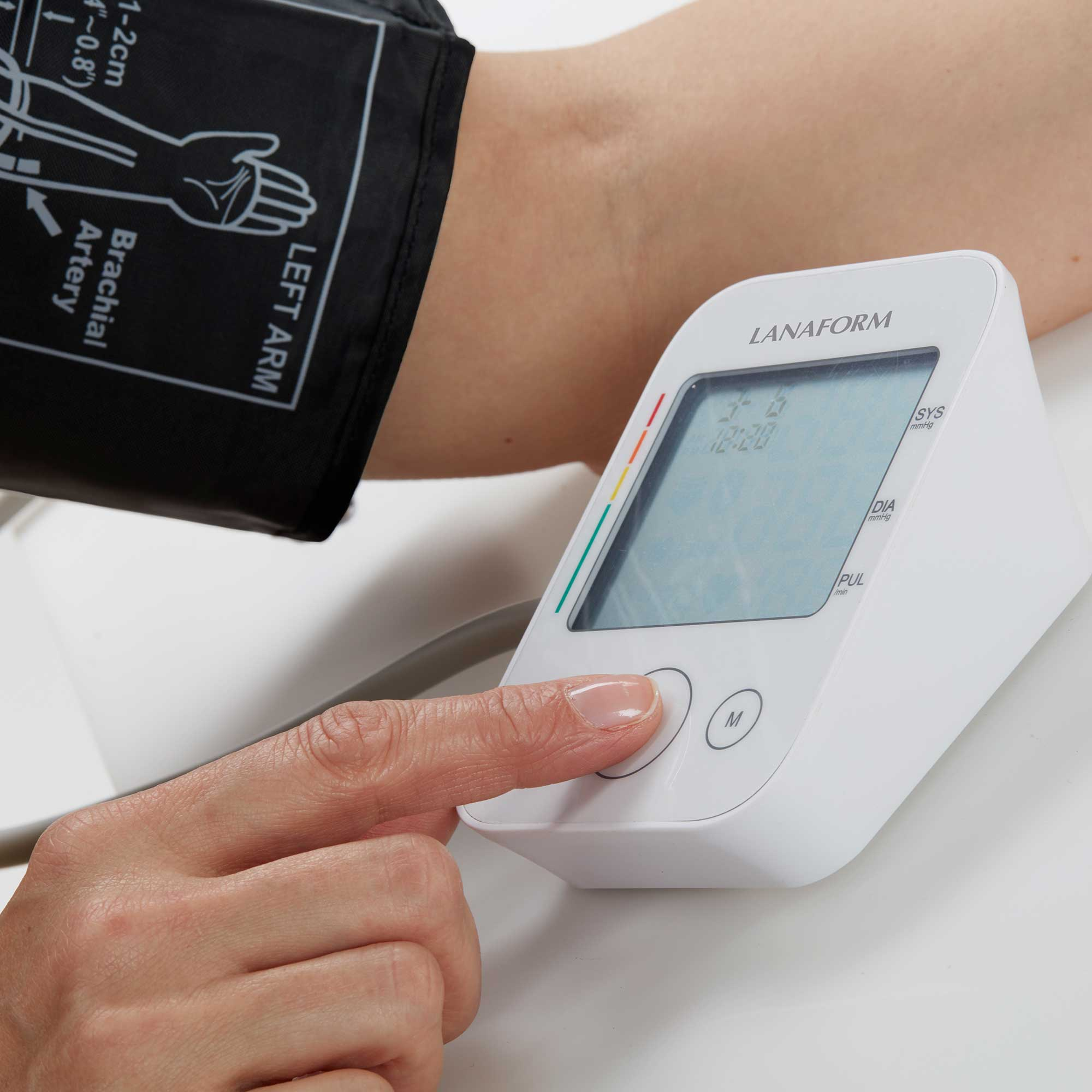 Arm einer Person mit Blutdruckmanschette. Ein weißes Blutdruckmessgerät davor.