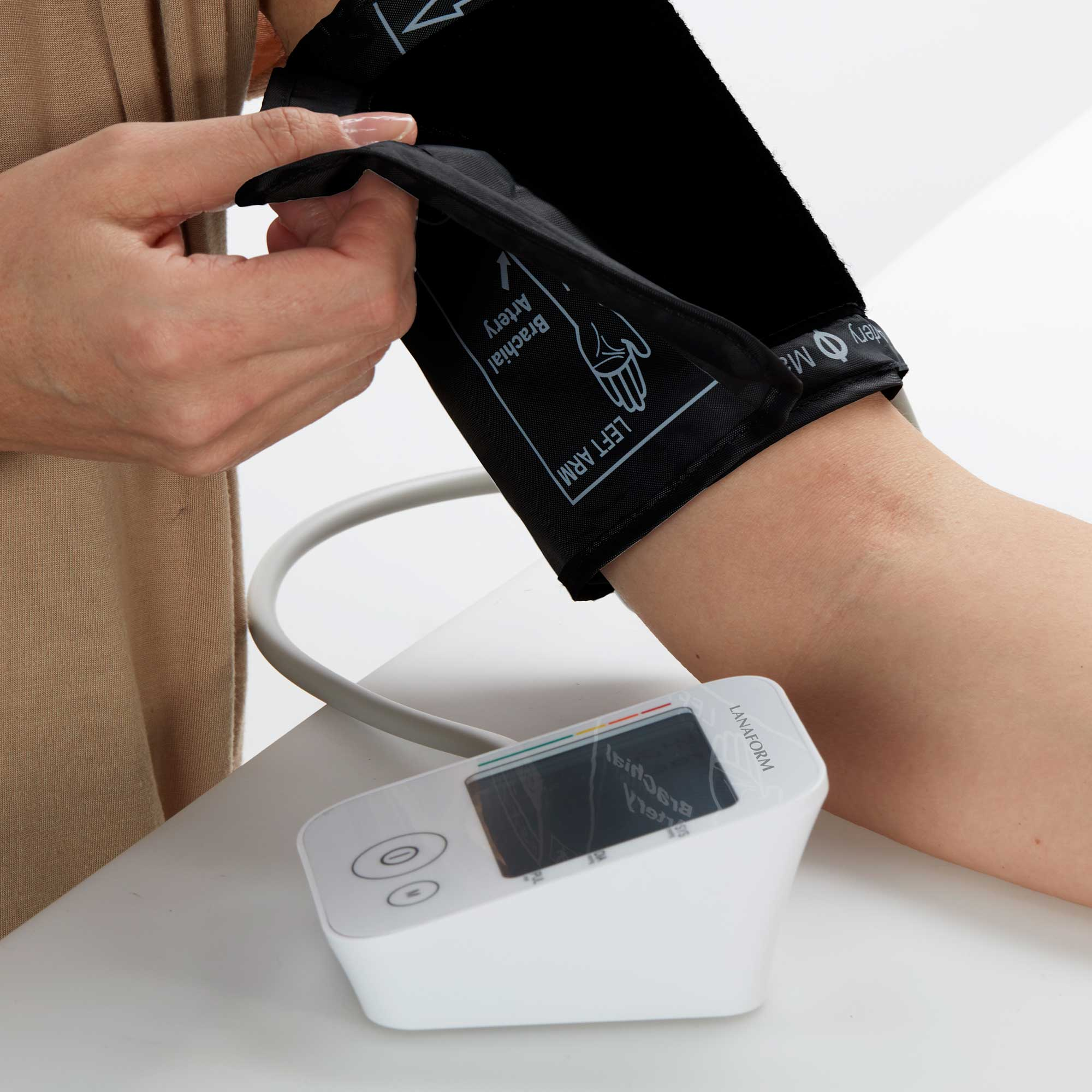 Arm einer Person mit Blutdruckmanschette und weißem Blutdruckmessgerät.