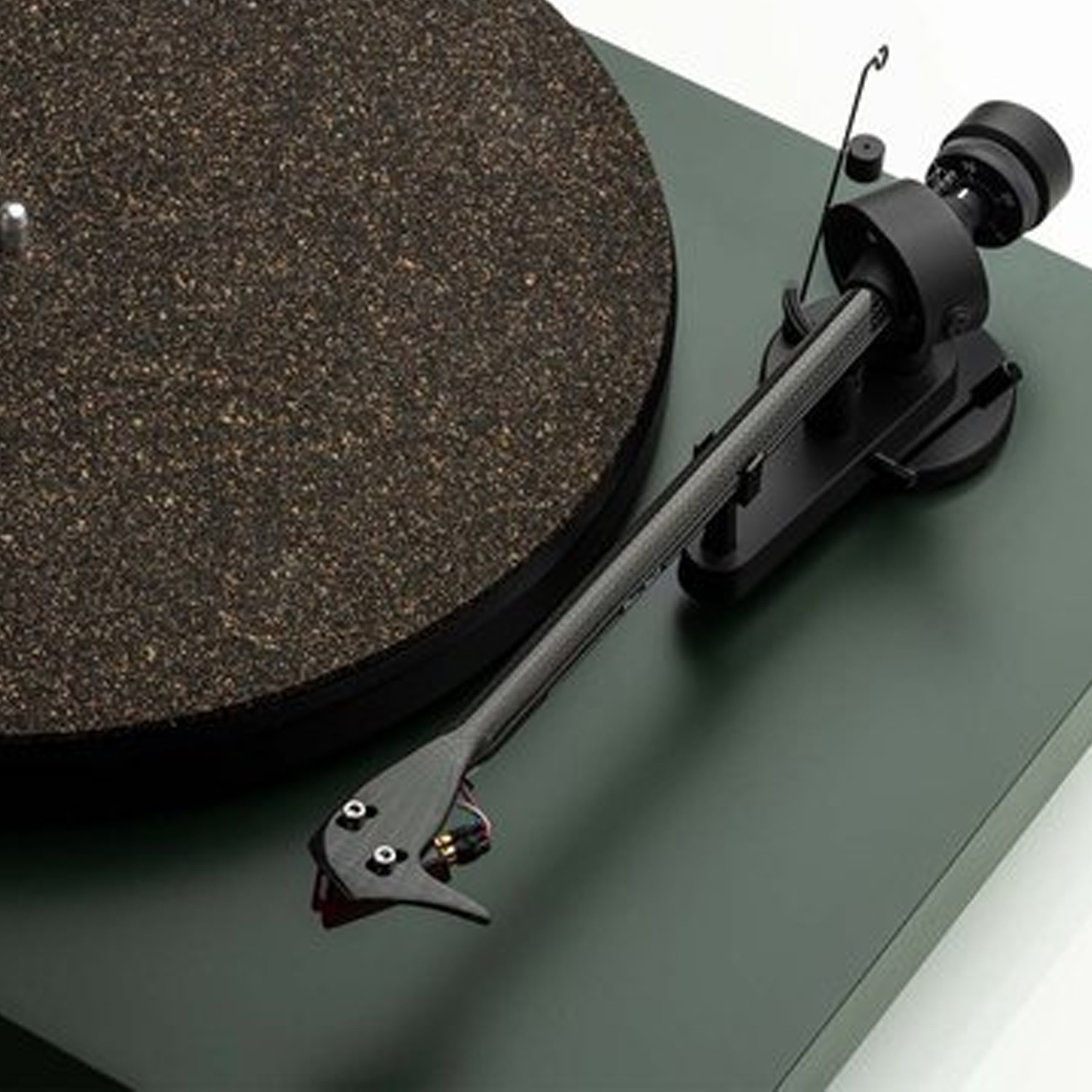 A turntable with a black arm and a round, dark-colored record on a green base.