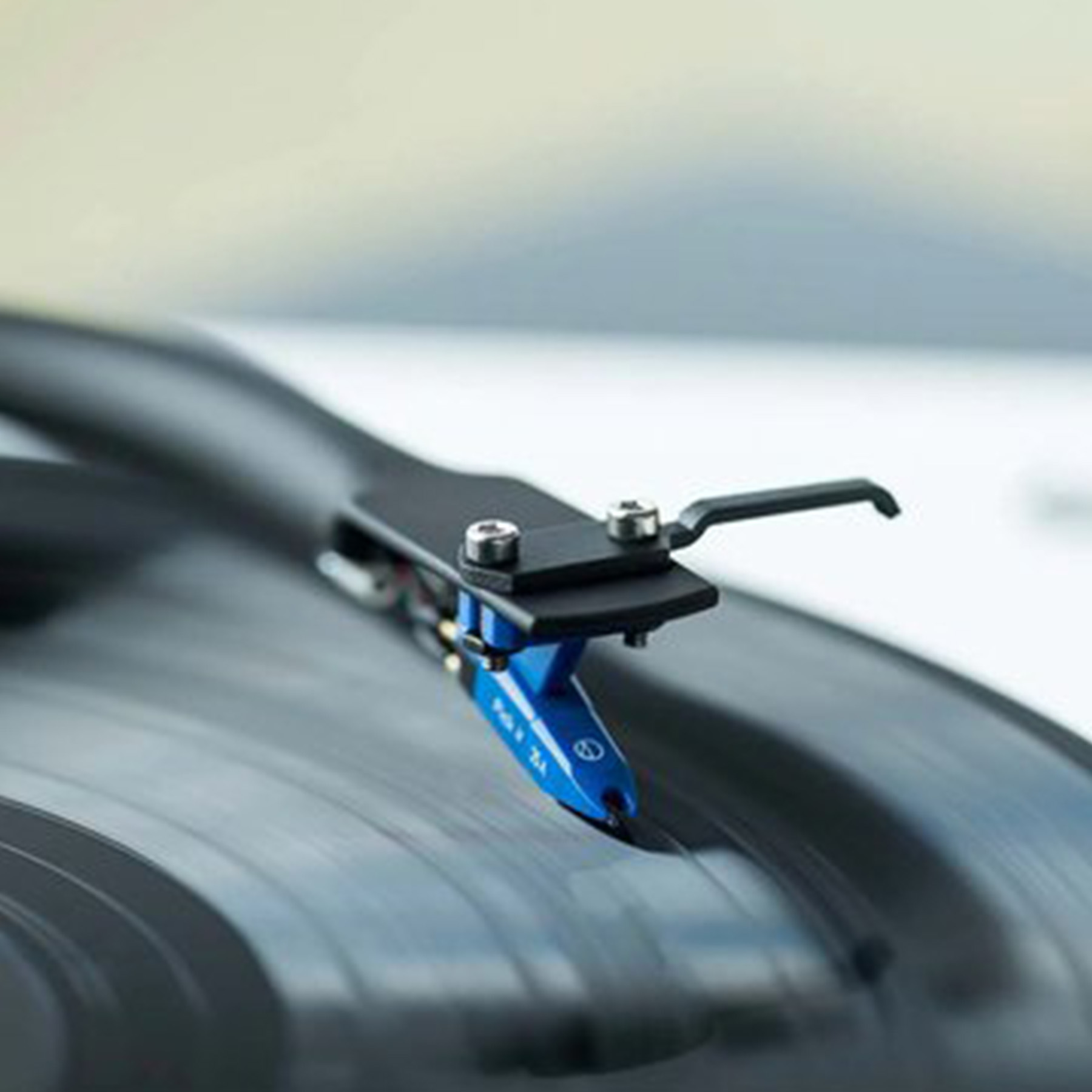 Zbliżenie igły gramofonowej na czarnej płycie winylowej. Igła jest niebieska i czarna.